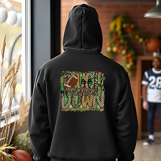 Person wearing a black hoodie with a festive design, standing in a room with autumn decorations.