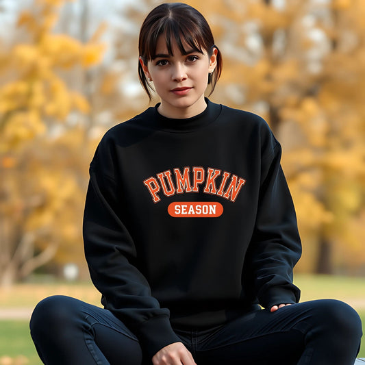 Person wearing a black sweatshirt with 'Pumpkin Season' text in an outdoor setting with trees in the background.