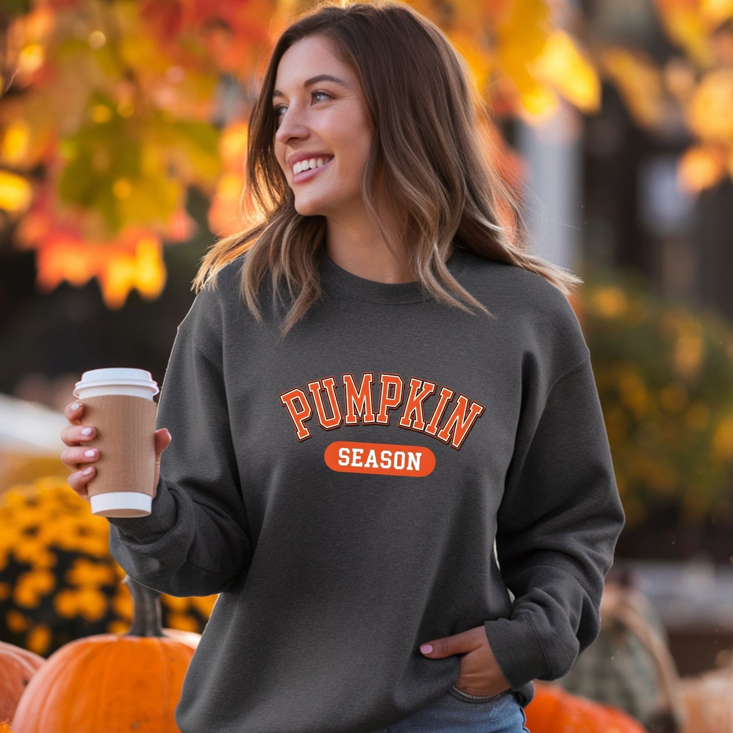 Woman wearing a 'Pumpkin Season' sweatshirt holding a coffee cup in an autumn setting.