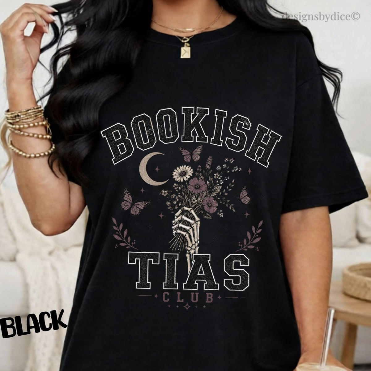 A woman wearing a black graphic T-shirt with the words 'BOOKISH TIAS CLUB' and a floral moon design, photographed indoors against a light neutral background.