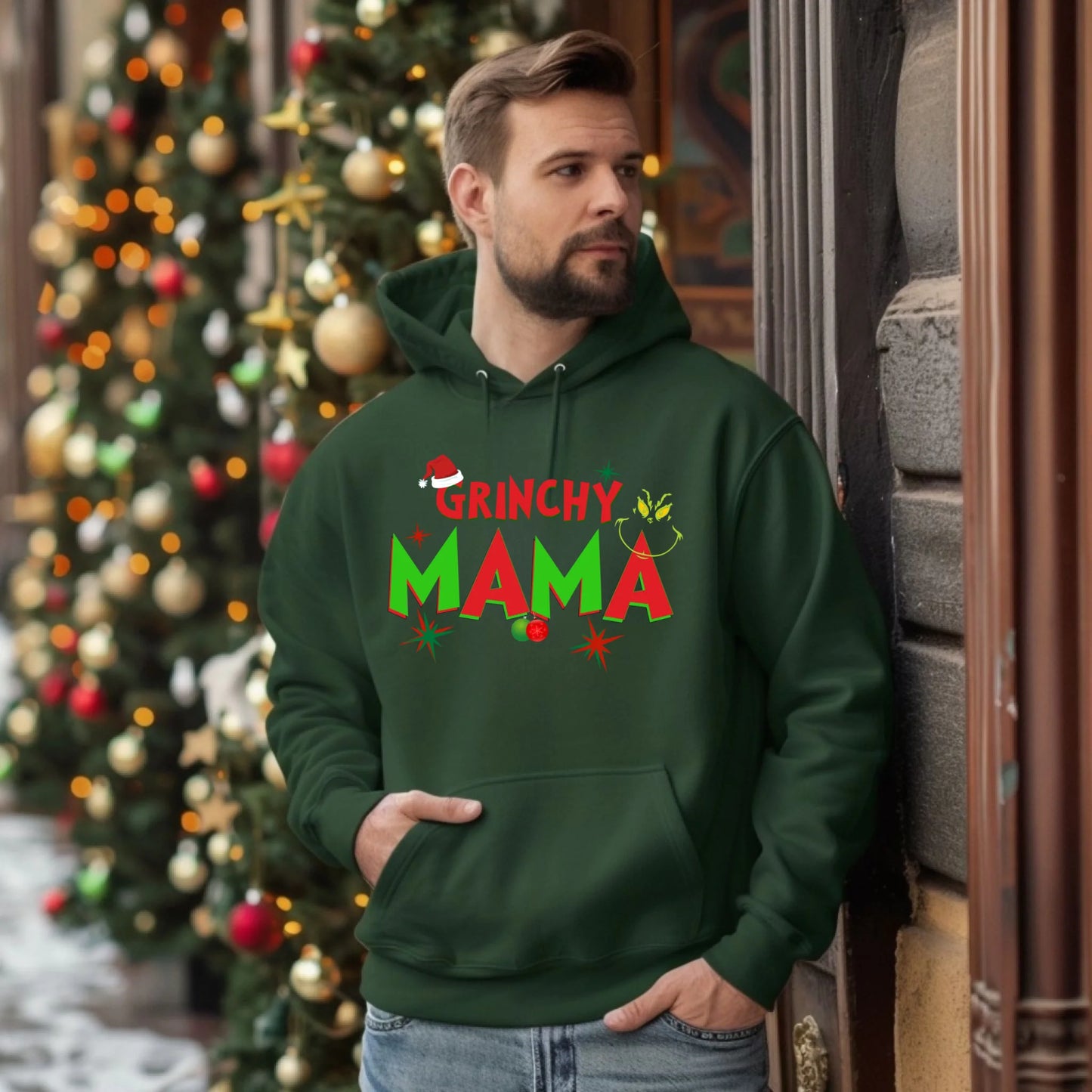 Man wearing a green 'Grinchy Mama' hoodie in front of a decorated Christmas tree.