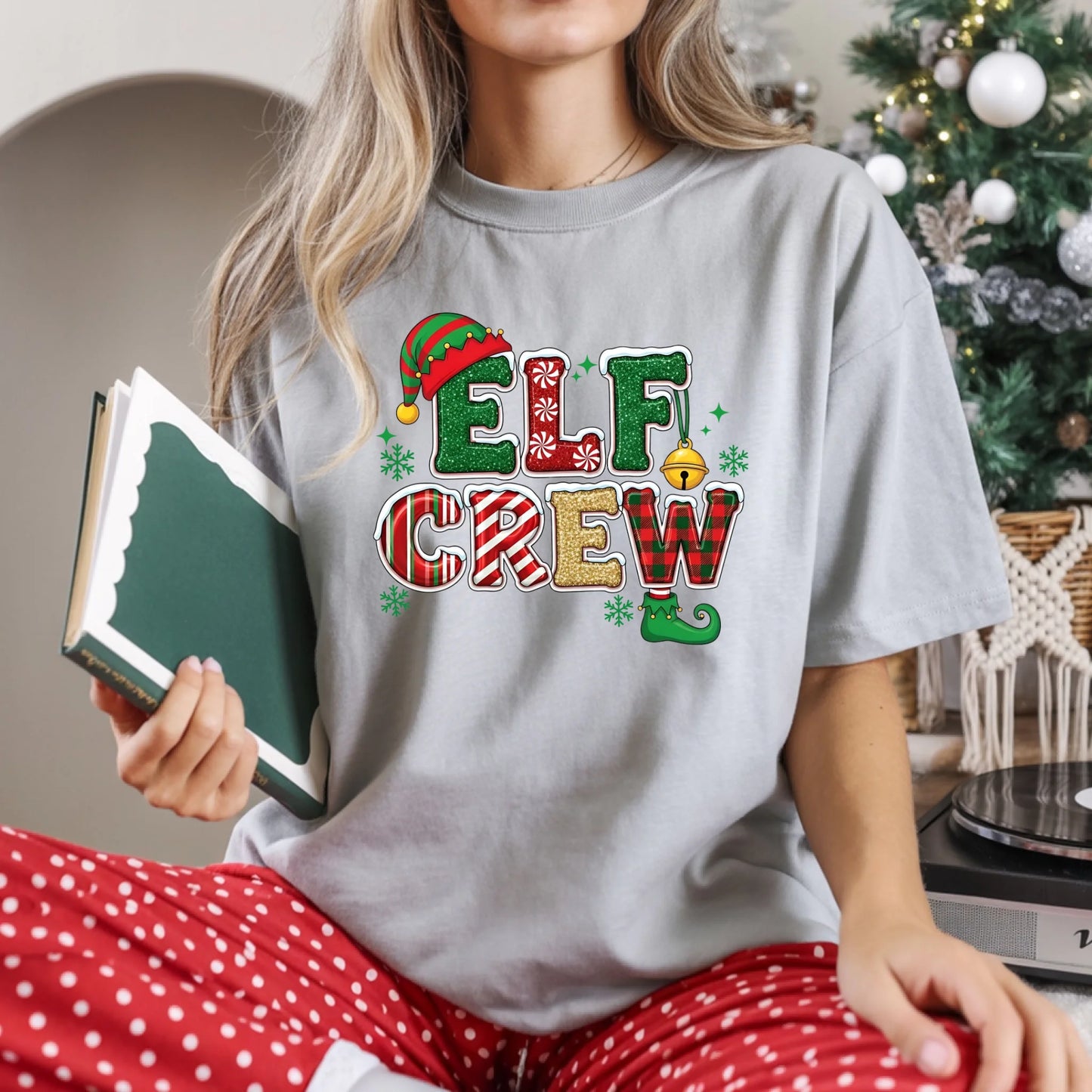 Person wearing a 'Elf Crew' t-shirt with a Christmas tree in the background