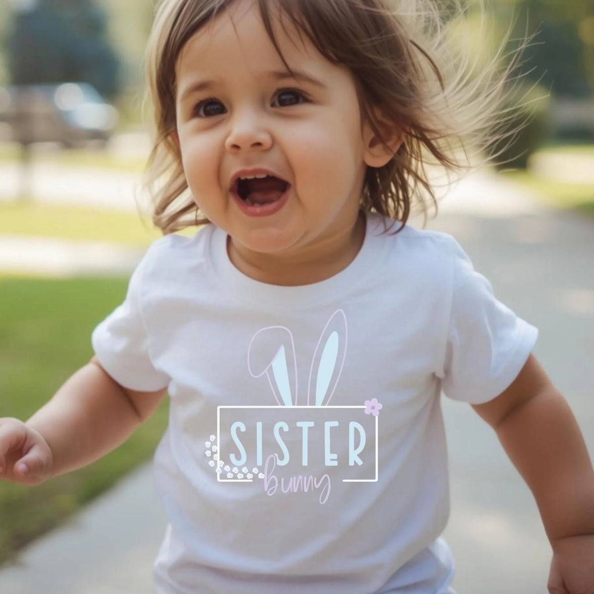 Toddler wearing a white Easter bunny sister t-shirt outdoors with a joyful expression.