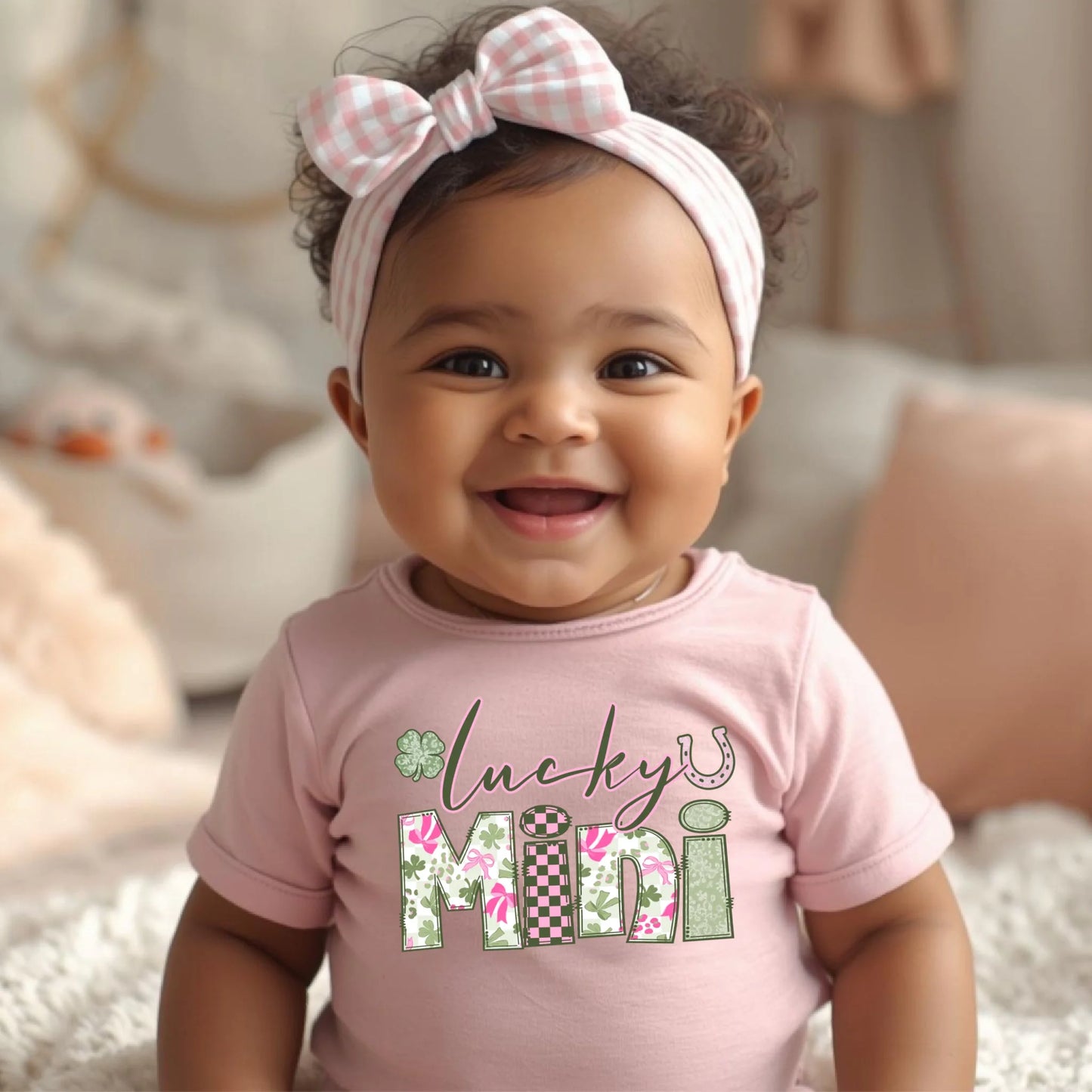 Baby wearing a pink shirt with 'lucky mini' text and a checkered bow headband.
