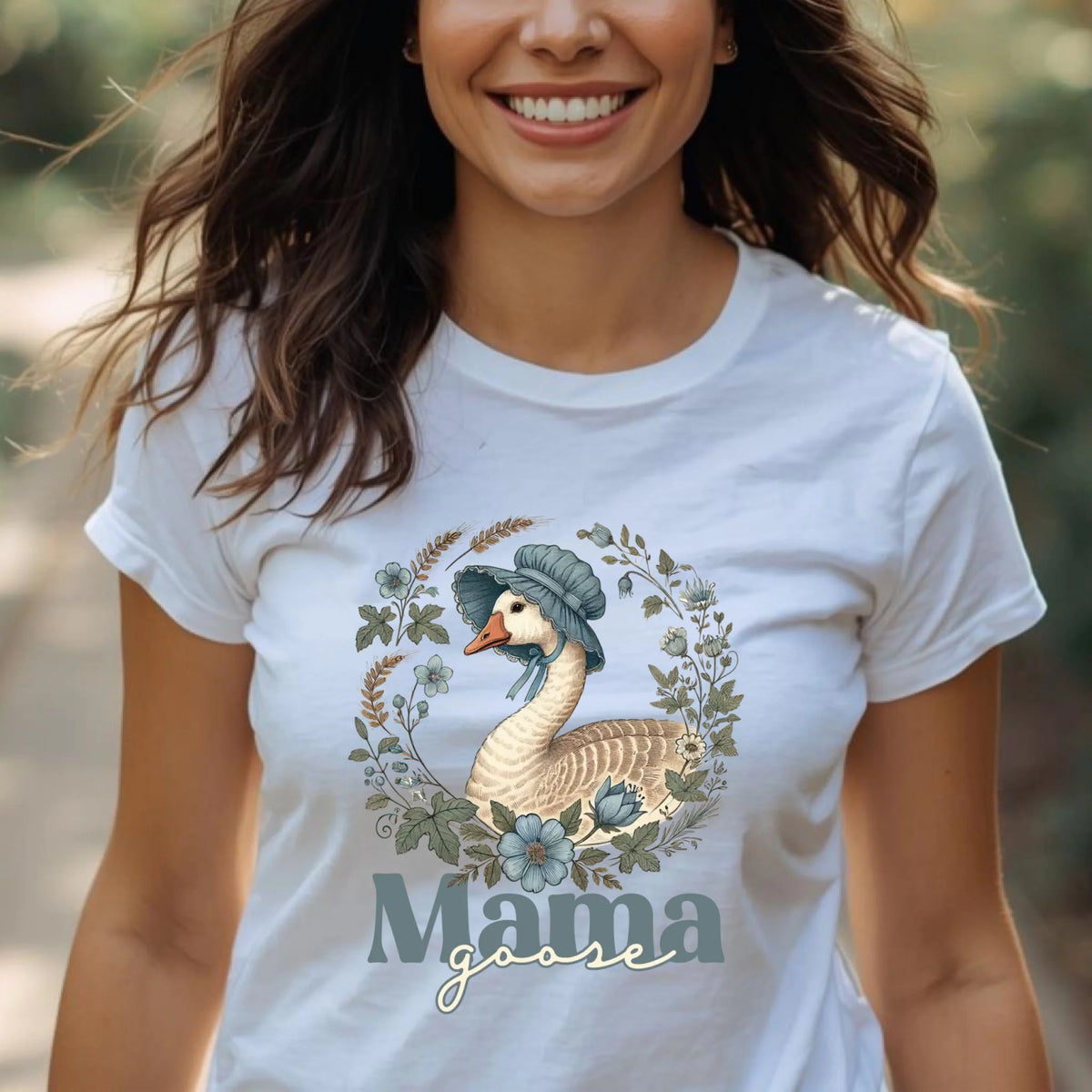Woman wearing a white Mama Goose floral t-shirt outdoors, featuring a vintage goose illustration surrounded by soft blue and sage florals, styled casually for everyday wear.