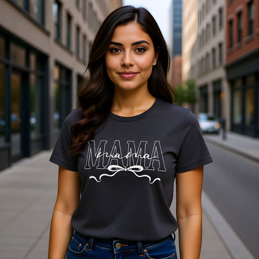 Woman wearing a dark grey Mama bow script t-shirt styled casually outdoors, showcasing a modern minimalist mom aesthetic.