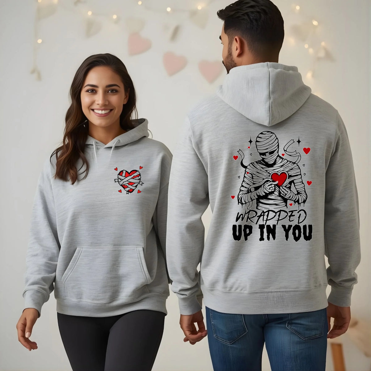 Two people wearing matching gray hoodies with heart-themed designs.