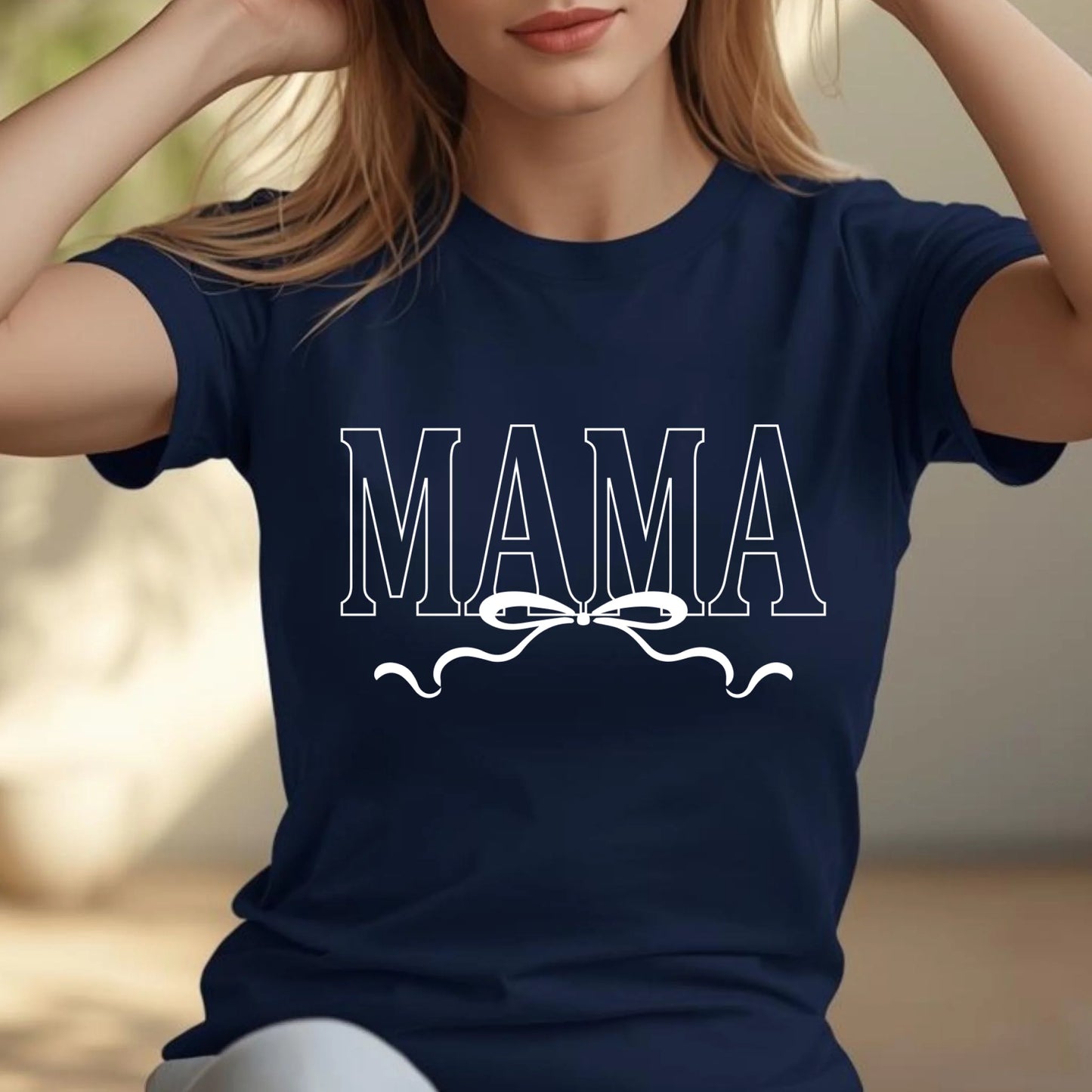 Navy blue t-shirt with 'MAMA' text and bow design worn by a person.