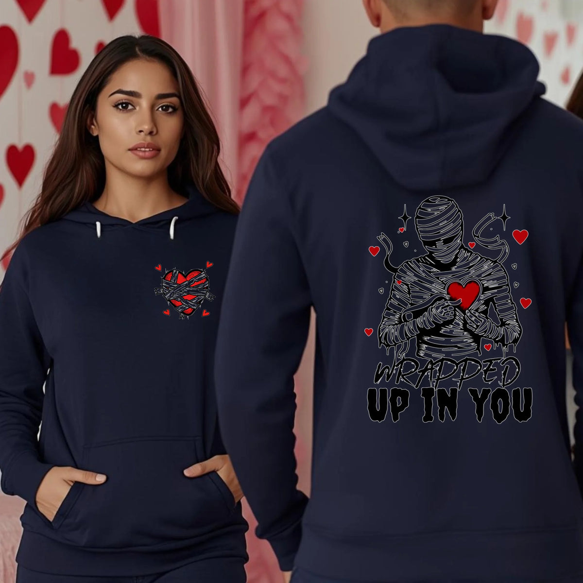 Two people wearing navy blue hoodies featuring the Wrapped Up In You mummy and heart back print along with a small wrapped heart chest graphic.