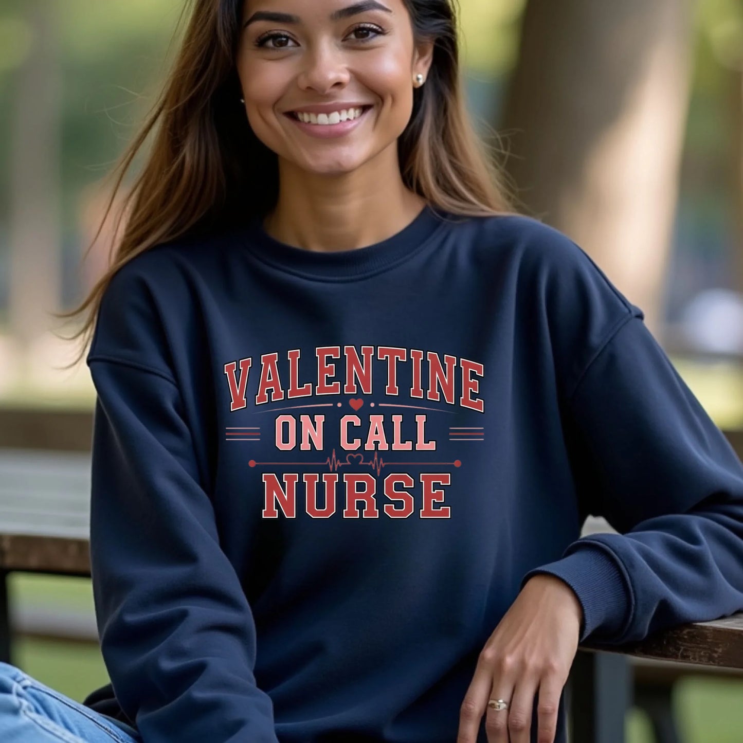 Woman wearing a navy Valentine On Call Nurse crewneck sweatshirt seated outdoors, highlighting a cozy fit and bold nurse graphic.