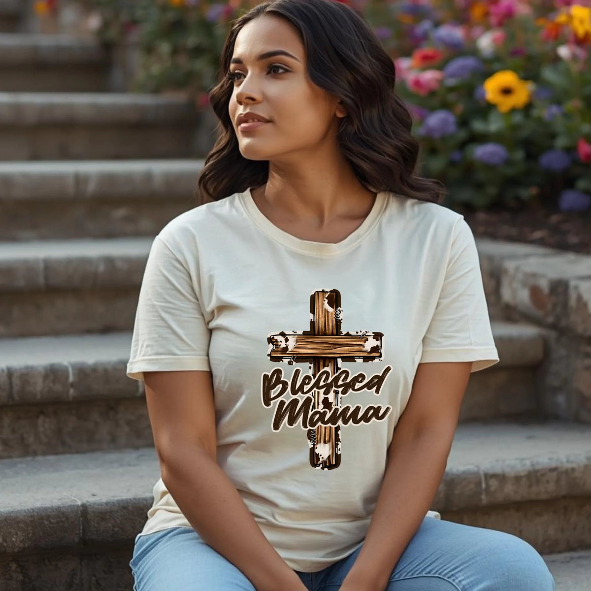 Woman wearing a cream Bella Canvas t-shirt with a Blessed Mama cross design, seated on outdoor steps in a natural lifestyle setting.