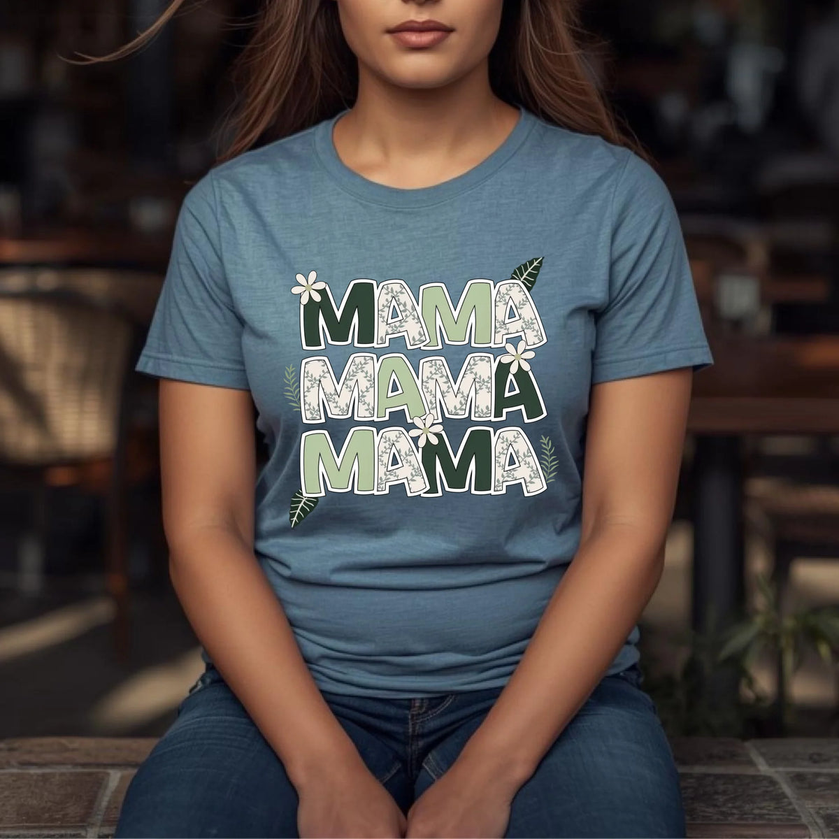 Woman seated outdoors wearing a blue floral “Mama” shirt styled for a relaxed everyday look.