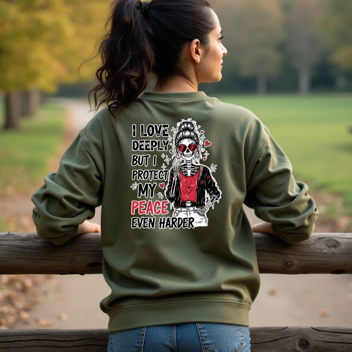 Military green crewneck sweatshirt with edgy Valentine skeleton design printed on the back, modeled in a park setting.
