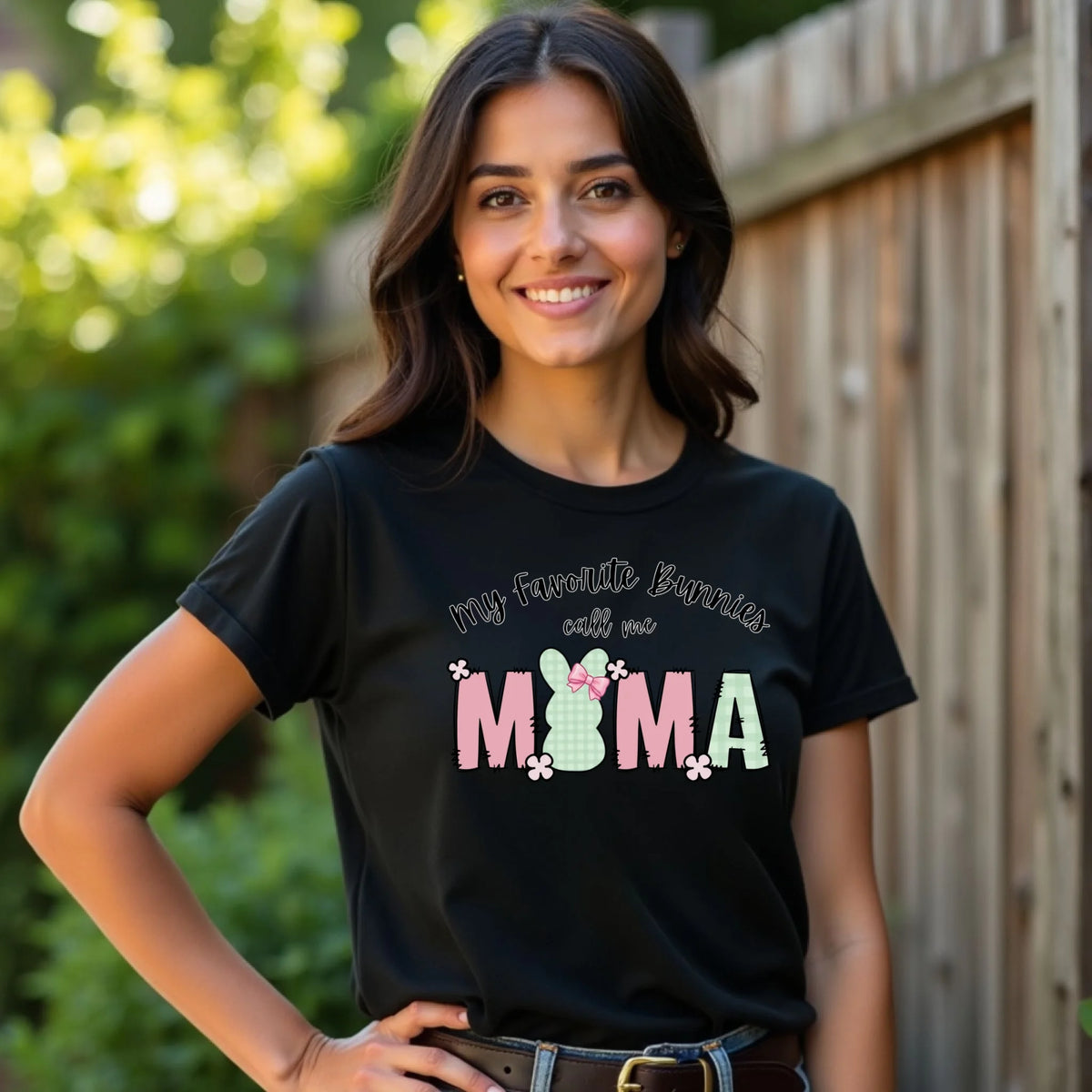 Woman standing outdoors wearing a black Bella Canvas t-shirt with a pastel Easter bunny “My Favorite Bunnies Call Me Mama” design.