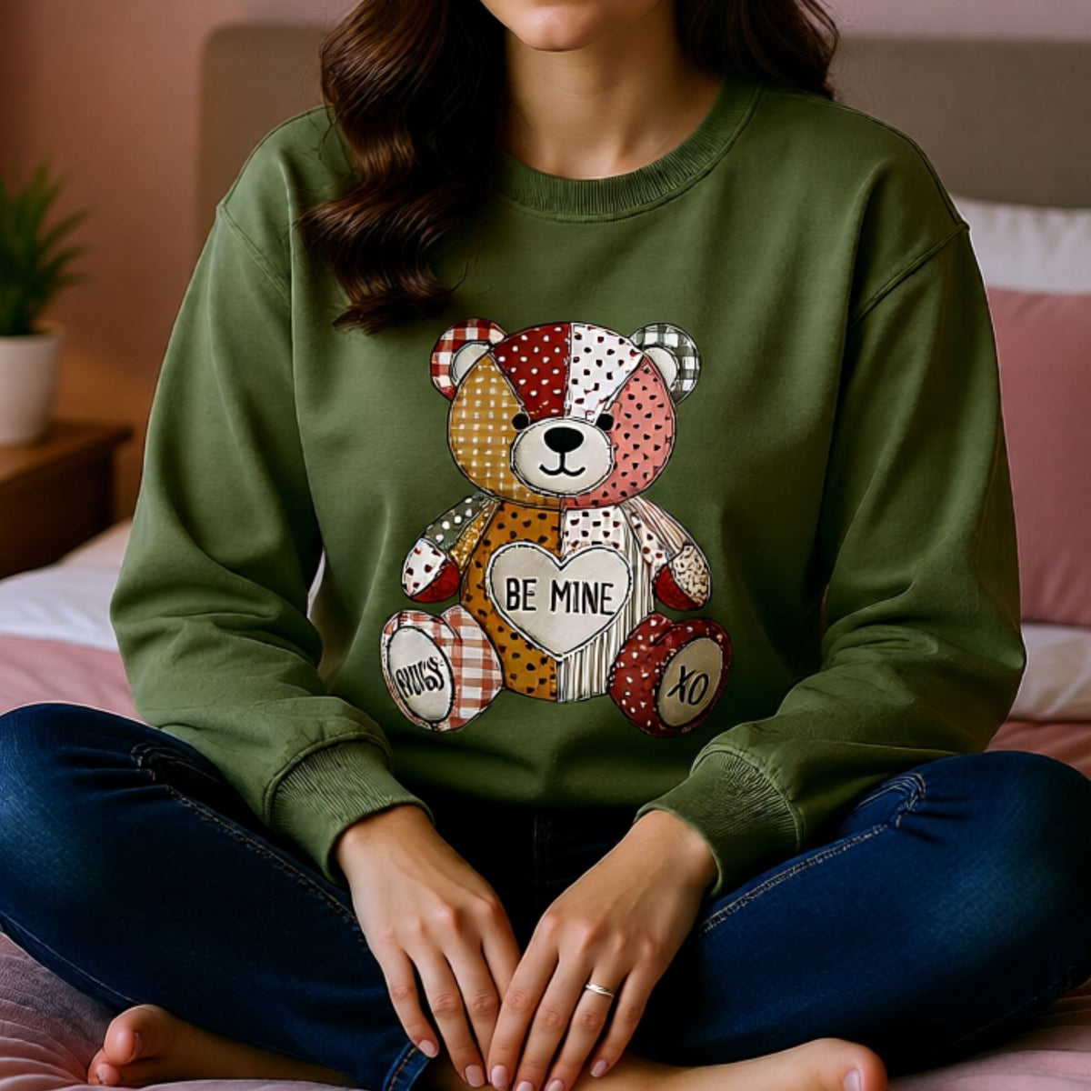 Woman wearing olive green Valentine crewneck with patchwork teddy bear holding heart that says Be Mine.