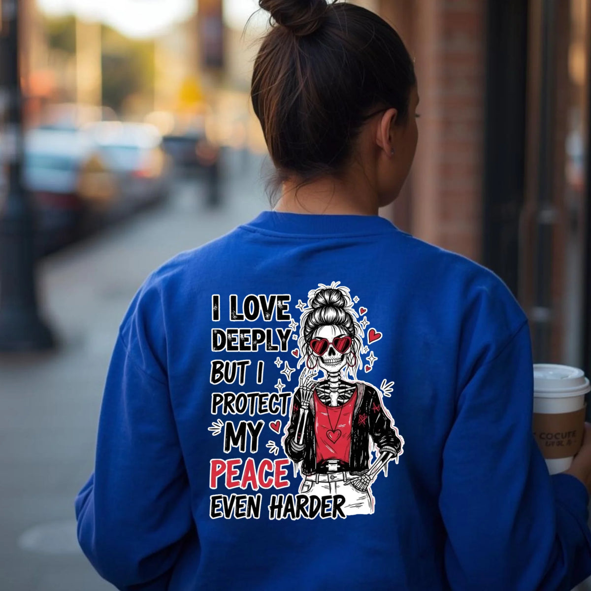 Royal blue crewneck sweatshirt with bold skeleton and heart back graphic, everyday streetwear setting with natural lighting.