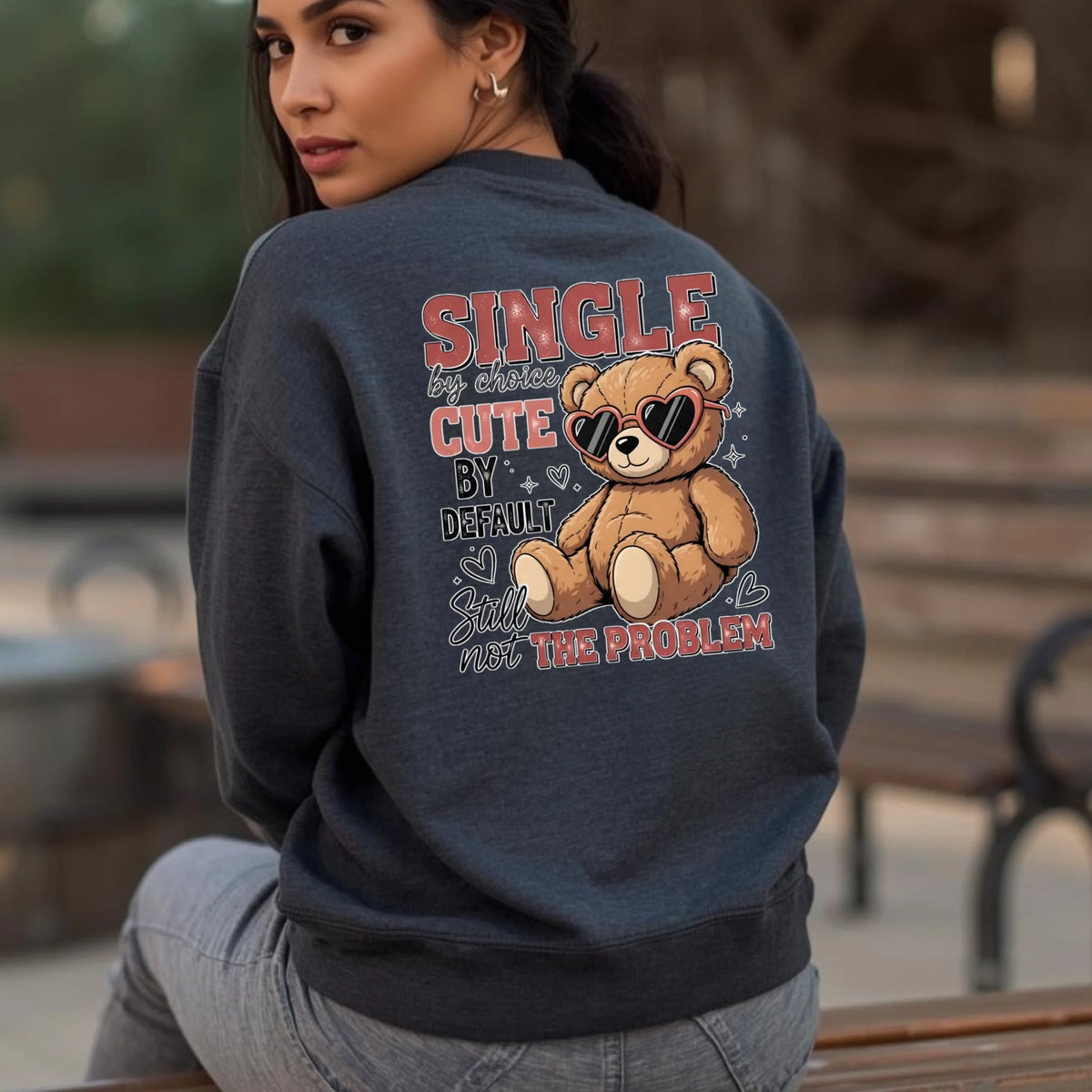Person wearing a navy sweatshirt with a teddy bear graphic and text outdoors.