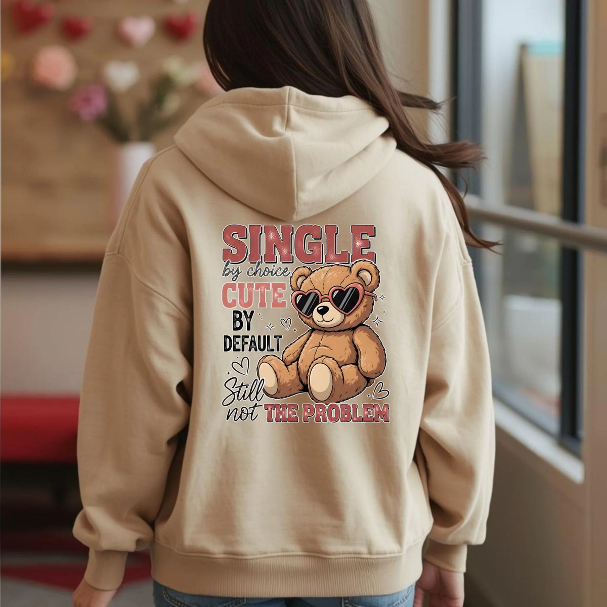Person wearing a beige hoodie with a teddy bear graphic and text on the back.