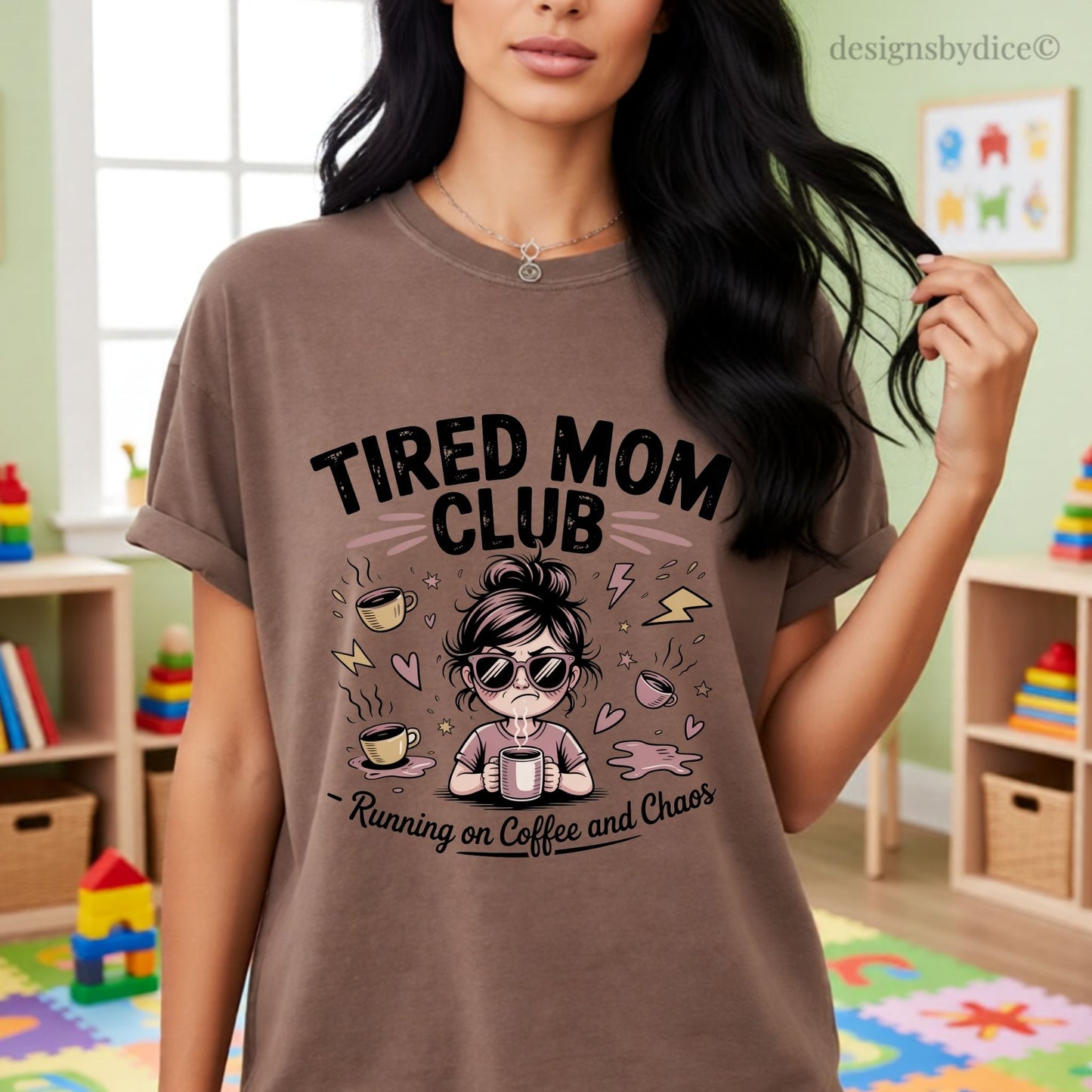 Woman wearing a brown t-shirt with 'Tired Mom Club' design in a room with children's toys.