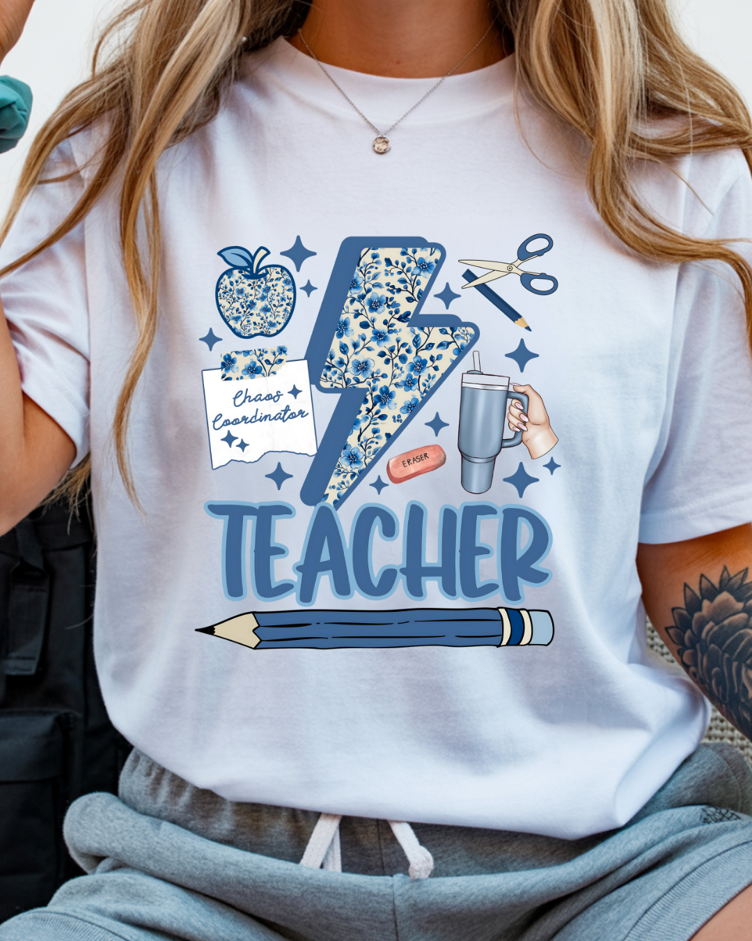White t-shirt with blue teacher-themed graphics and text worn by a person.