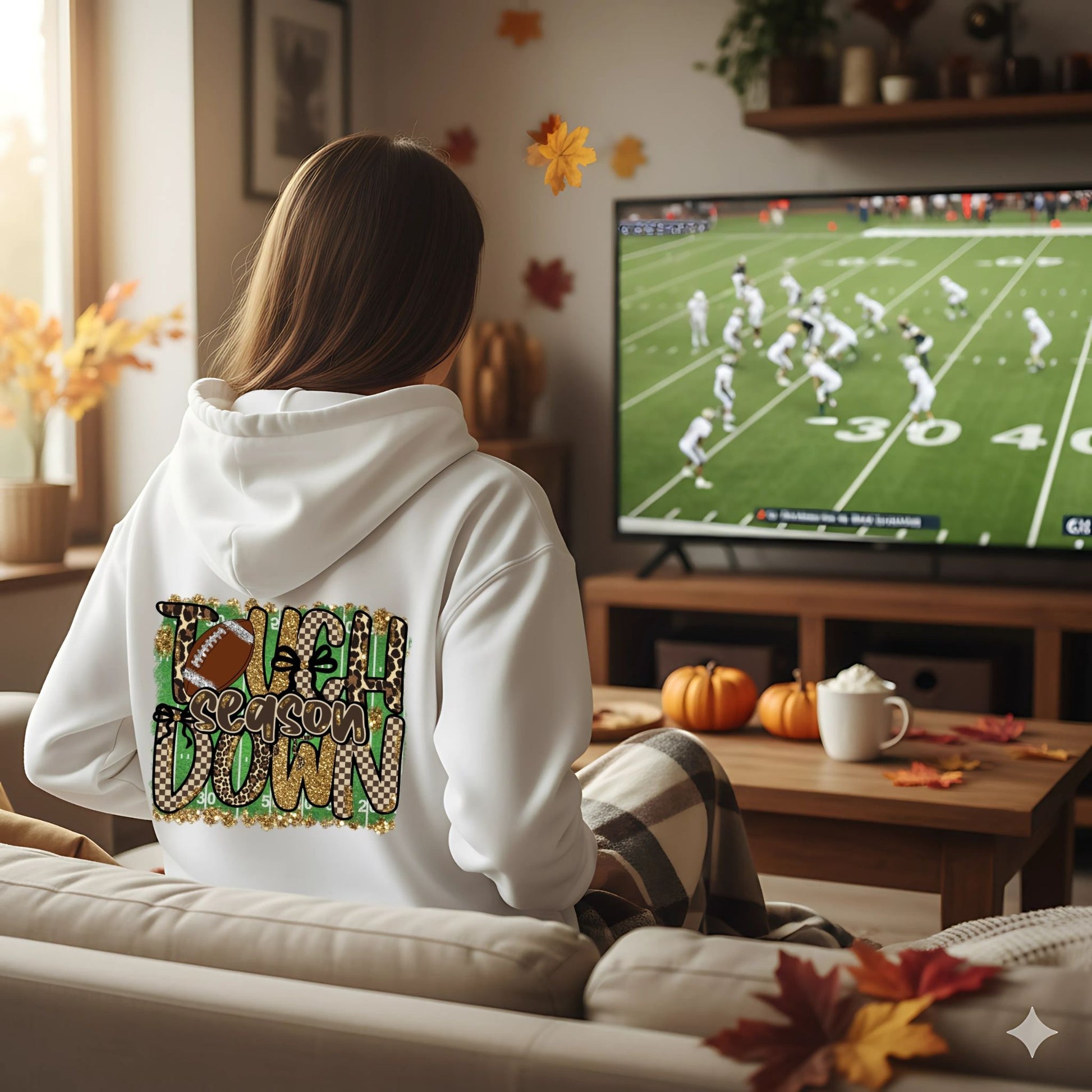 Person wearing a hoodie with 'Season Down' design, sitting on a couch watching football on TV.
