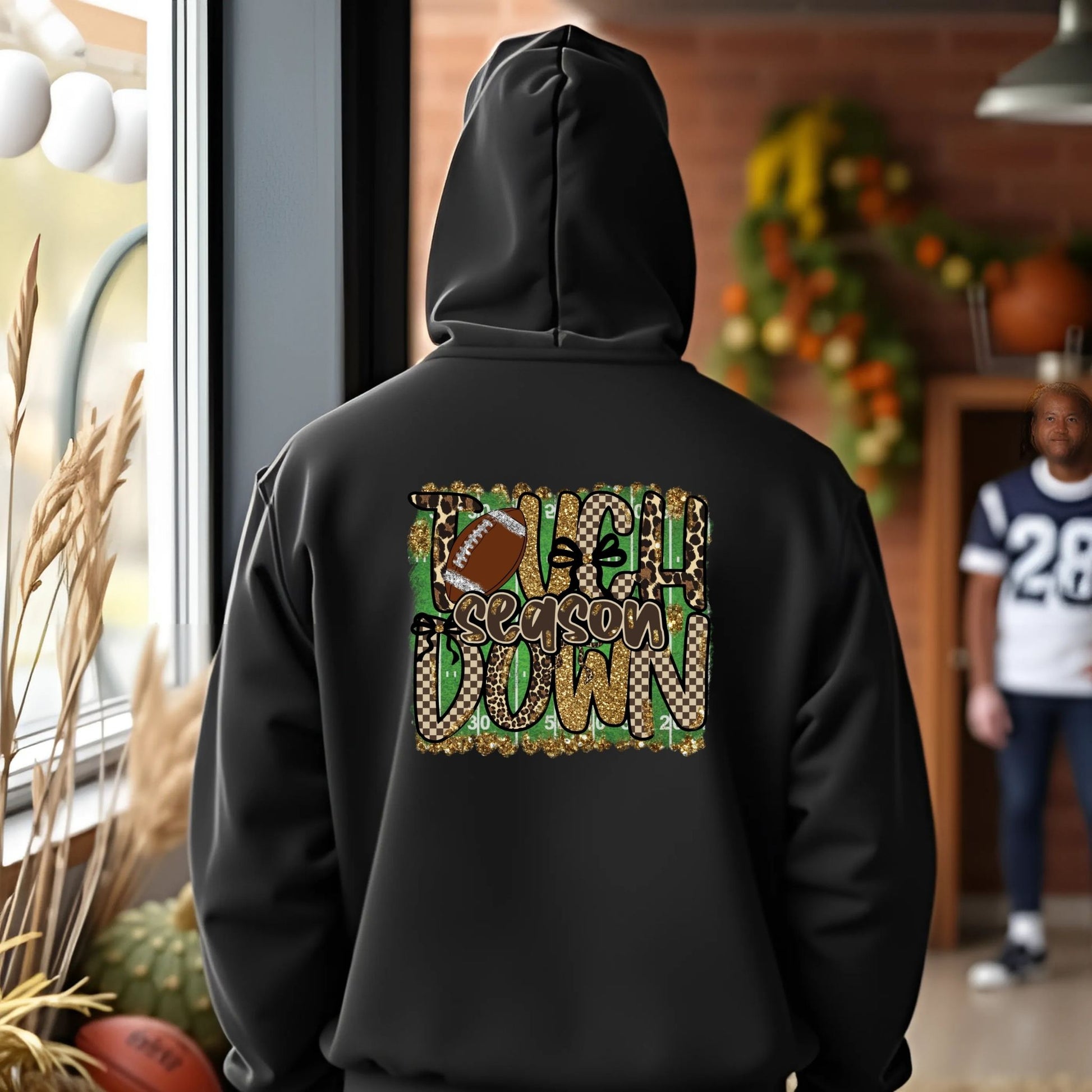Person wearing a black hoodie with a festive design, standing in a room with autumn decorations.