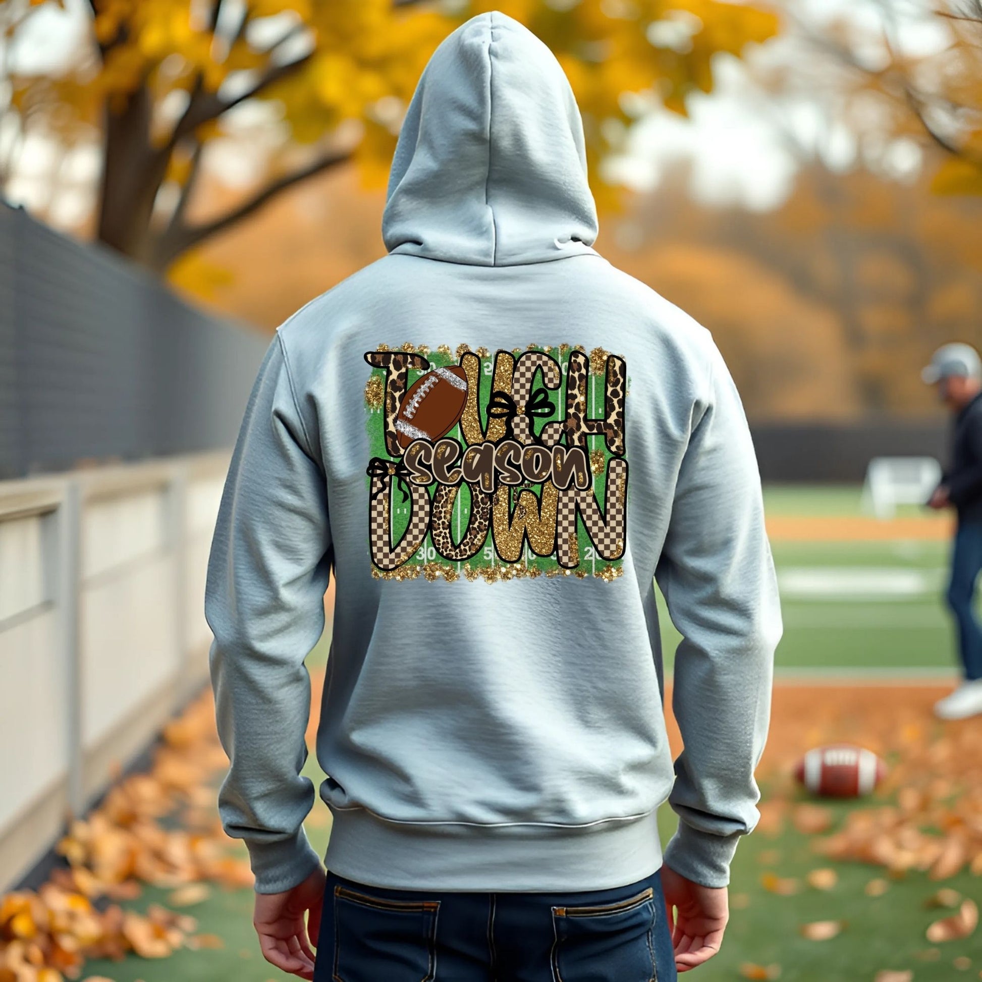 Person wearing a gray hoodie with 'Touchdown Season Down' design on the back, standing on a football field.