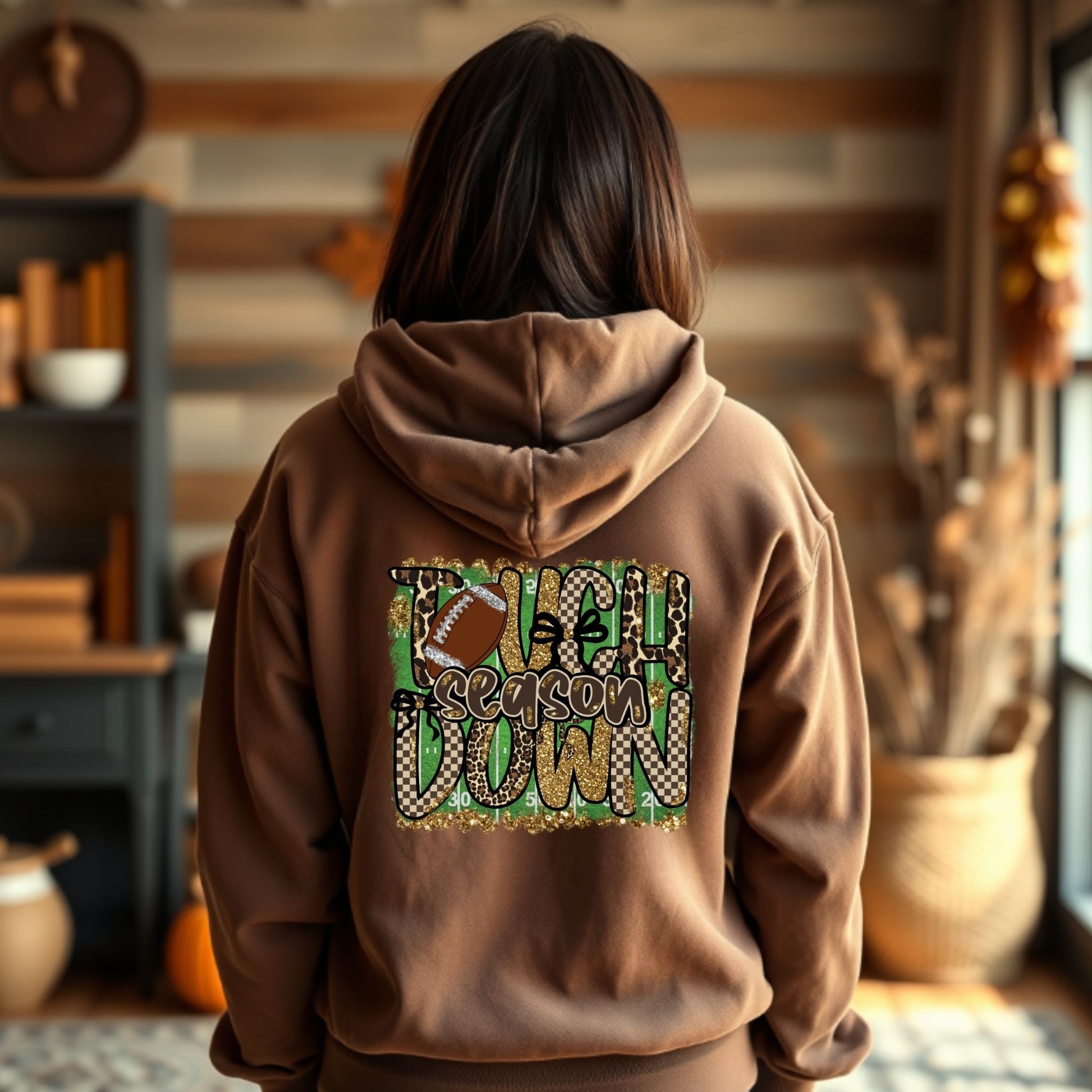 Person wearing a brown hoodie with 'Tailgating Season' text in a cozy indoor setting