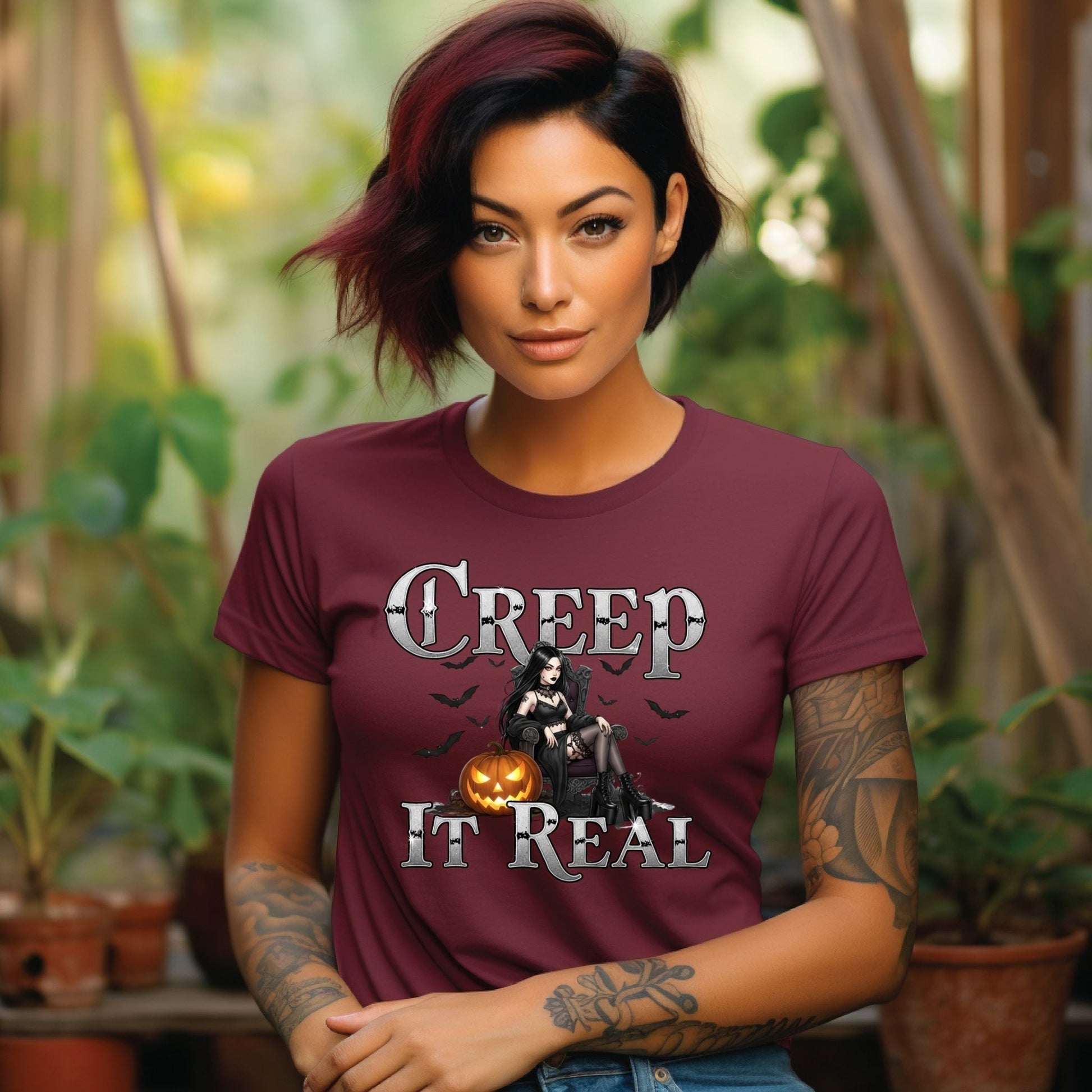 Person wearing a maroon t-shirt with a graphic design and text, standing outdoors with plants in the background.