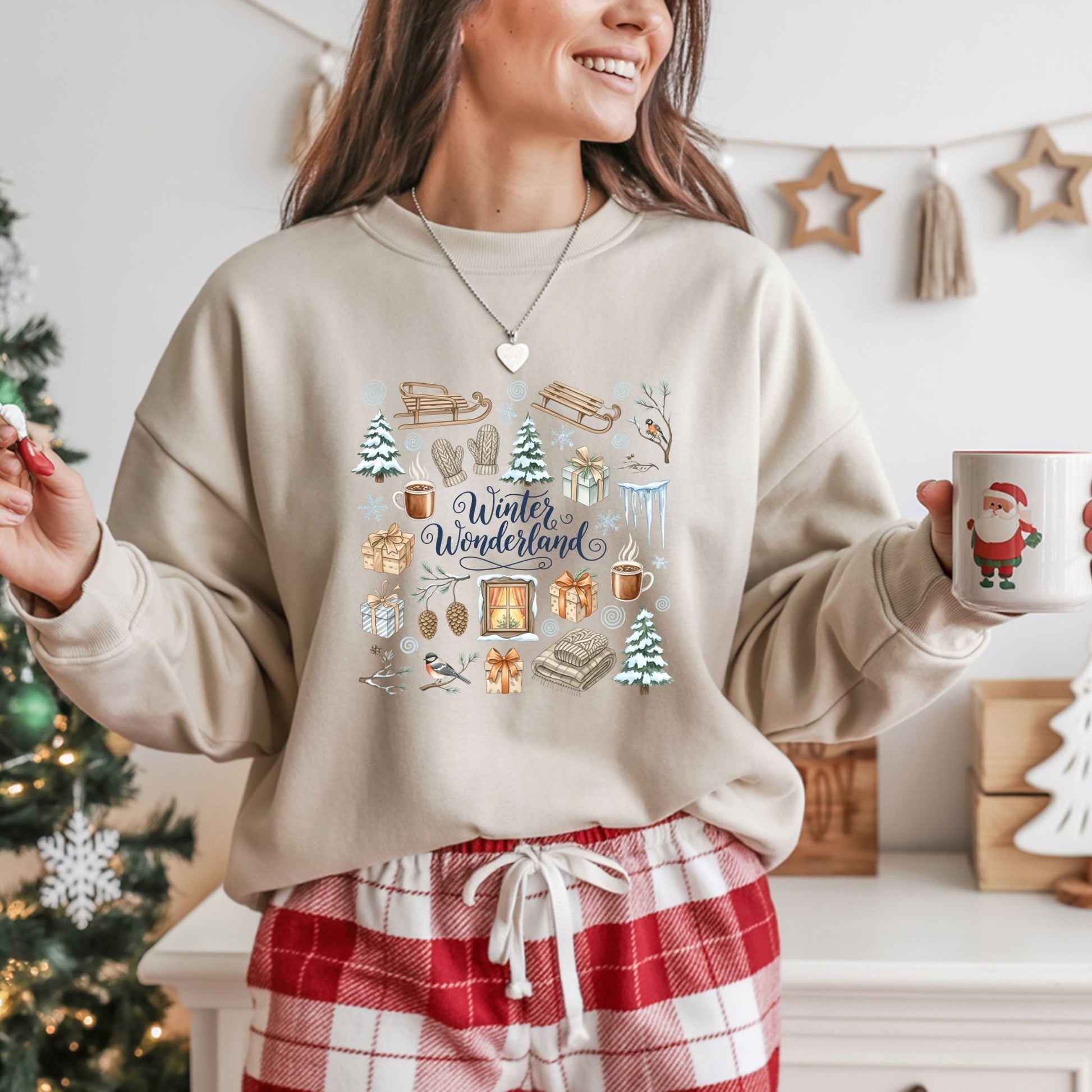 Person wearing a beige sweatshirt with winter-themed graphics and plaid pants, holding a mug in a festive setting.