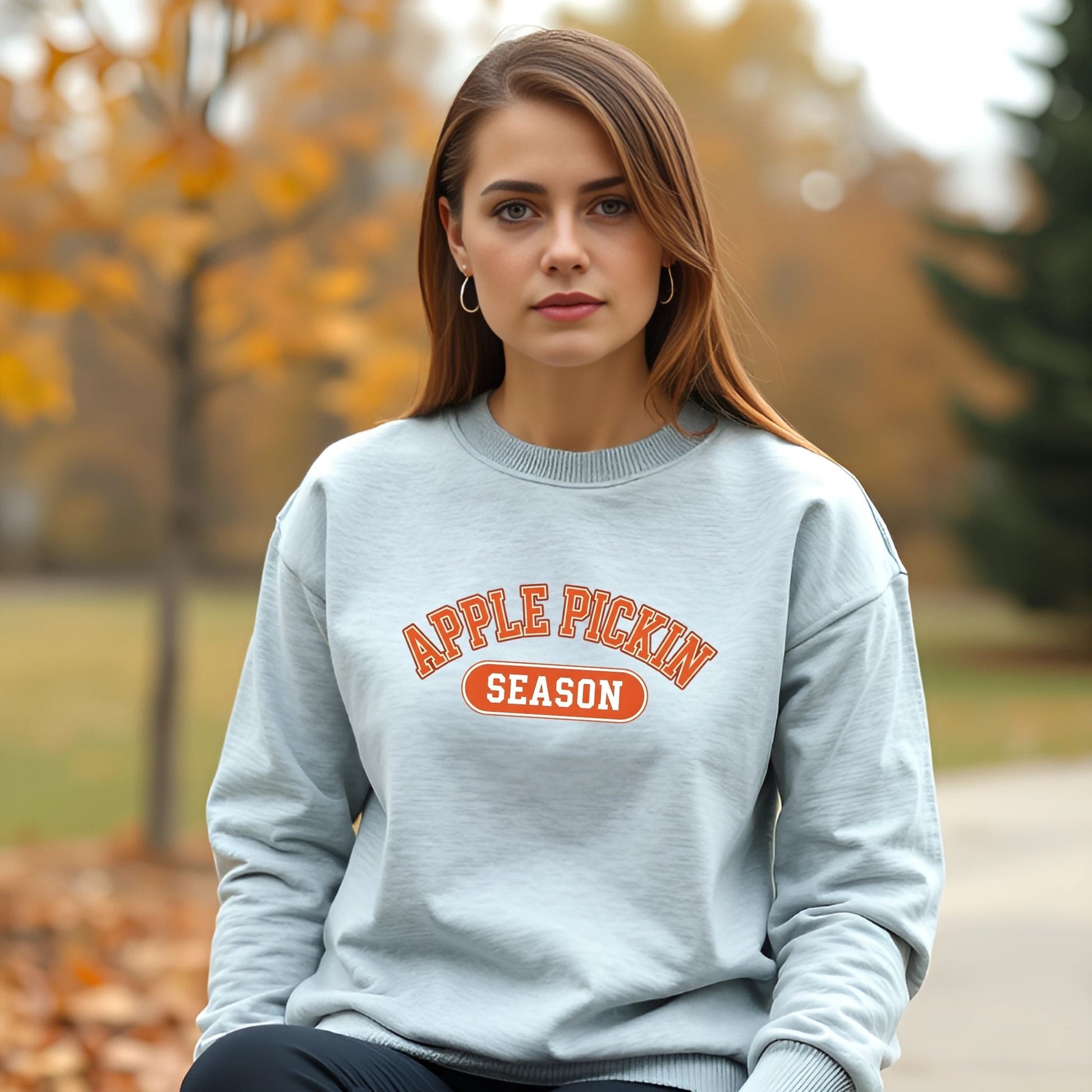 Woman wearing a gray sweatshirt with 'Apple Pickin' Season' text in an outdoor setting.