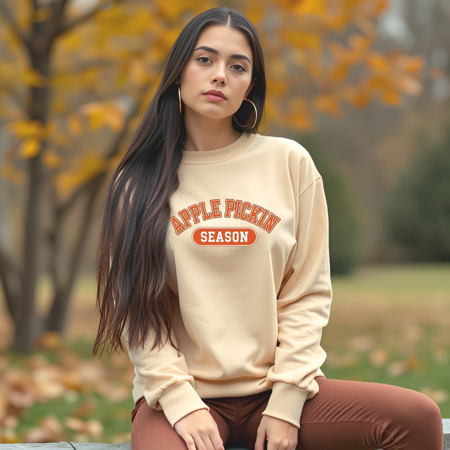 Woman wearing a beige sweatshirt with 'Apple Pickin' Season' text in an autumn setting