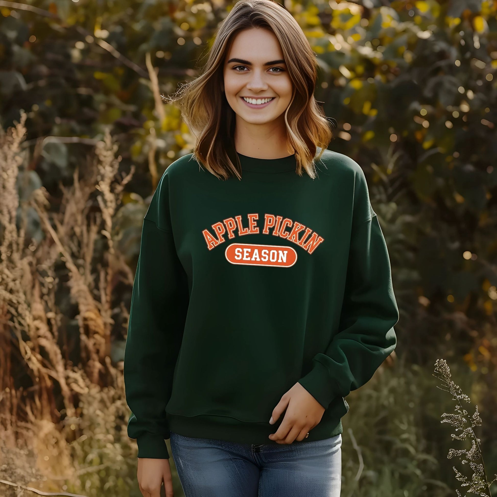 Woman wearing a green sweatshirt with 'Apple Pickin' Season' text in a field.