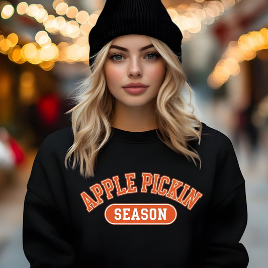 Person wearing a black sweatshirt with 'APPLE PICKIN SEASON' text against a blurred background