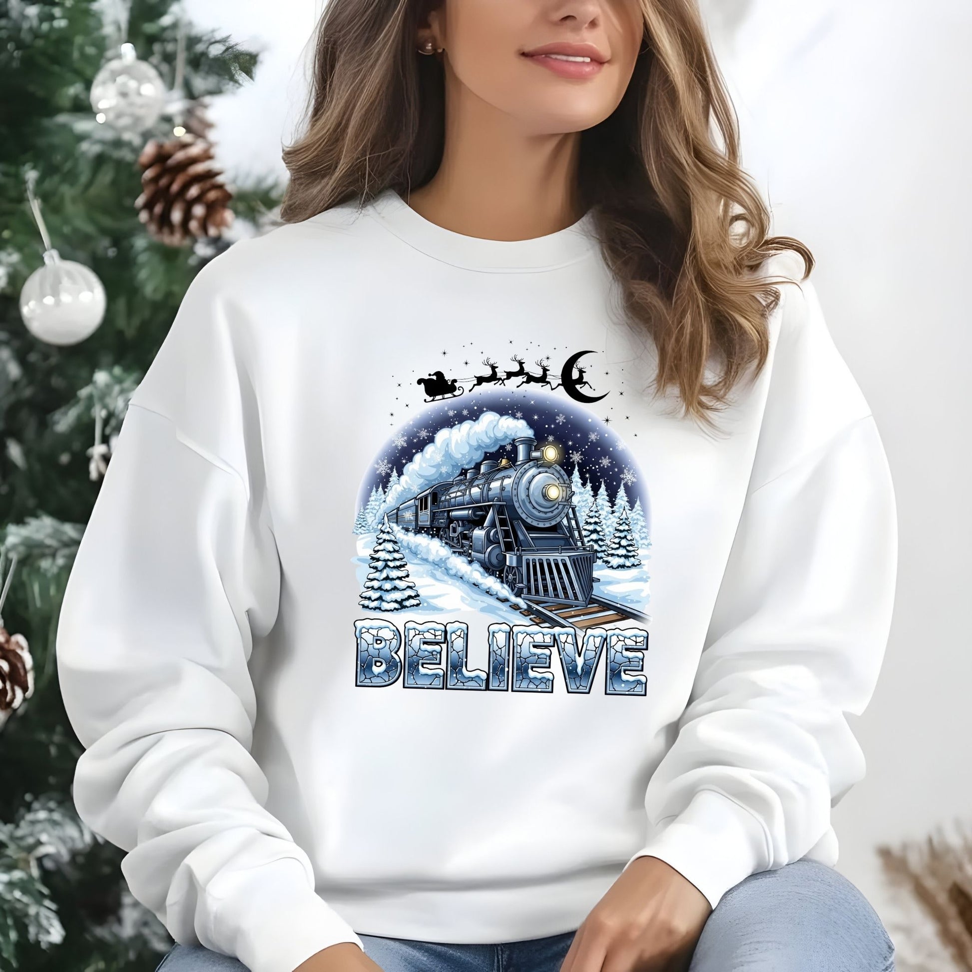 Person wearing a white sweatshirt with a Christmas-themed design featuring a train and 'BELIEVE' text, sitting in front of a decorated Christmas tree.