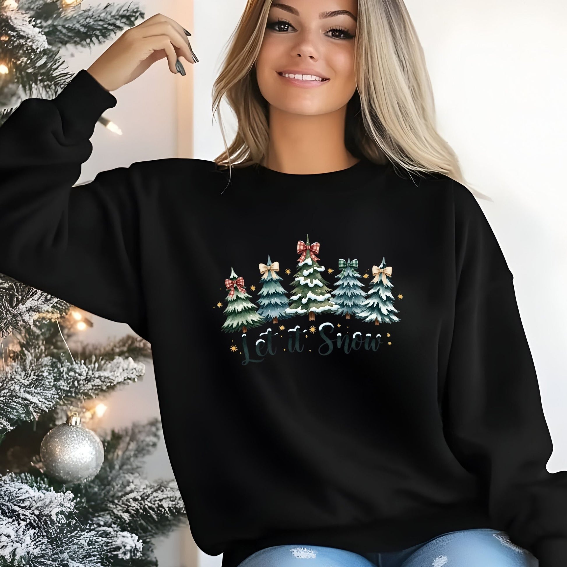 Person wearing a black sweater with Christmas tree design and 'Let it Snow' text, standing next to a decorated Christmas tree.