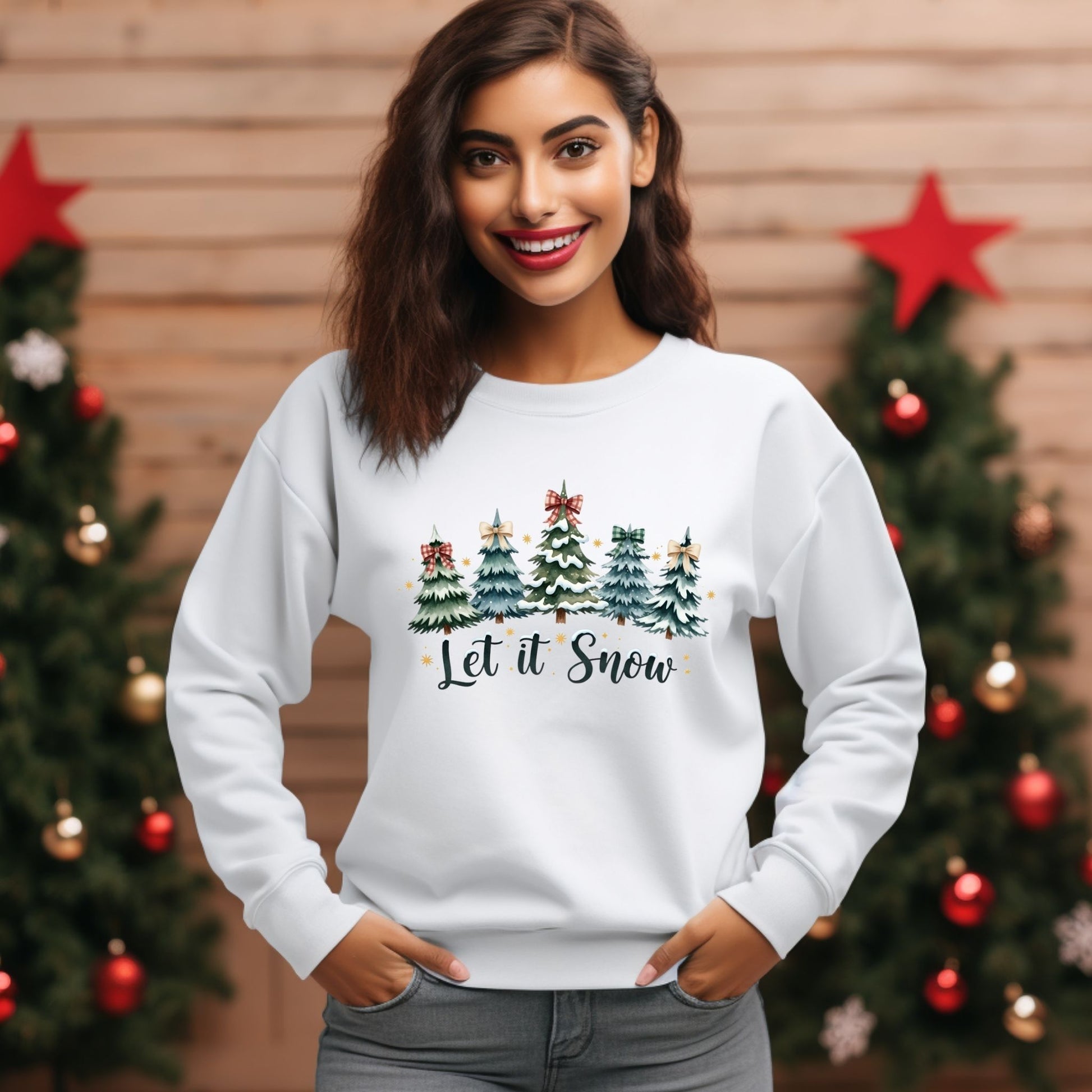 Woman wearing a white sweatshirt with Christmas tree design and 'Let it Snow' text, standing in front of decorated trees.
