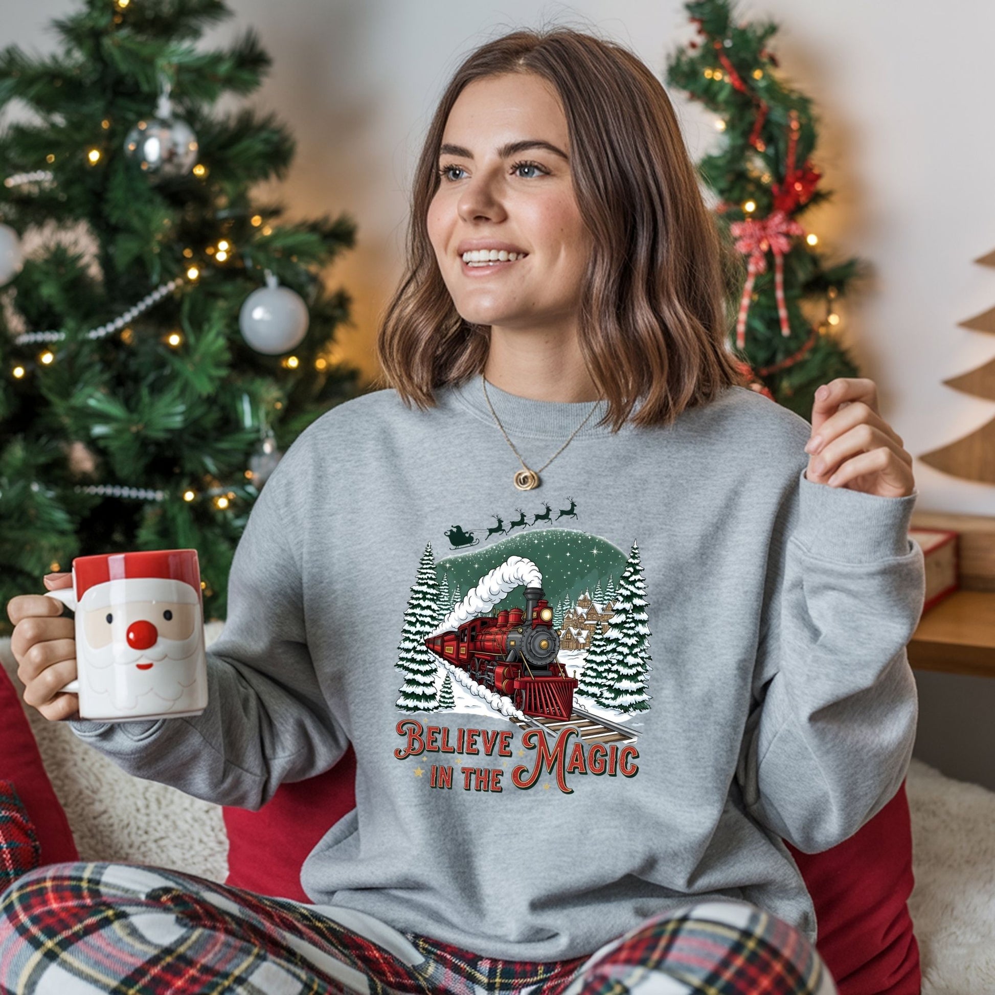 Woman wearing a Christmas-themed sweatshirt with a train and reindeer design, holding a mug in a festive setting.
