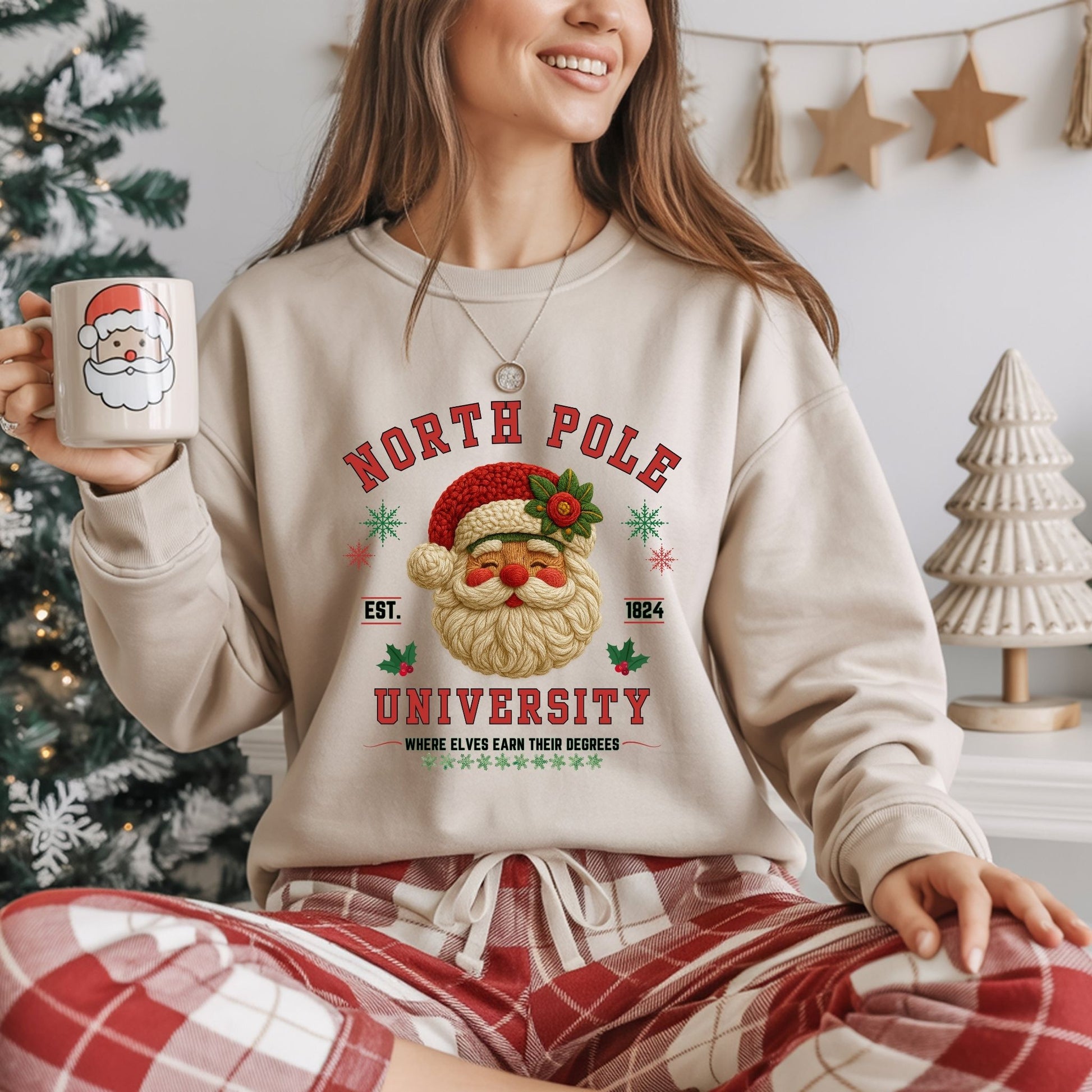 Person wearing a 'North Pole University' sweatshirt holding a mug with a Santa Claus design, sitting in a festive setting.