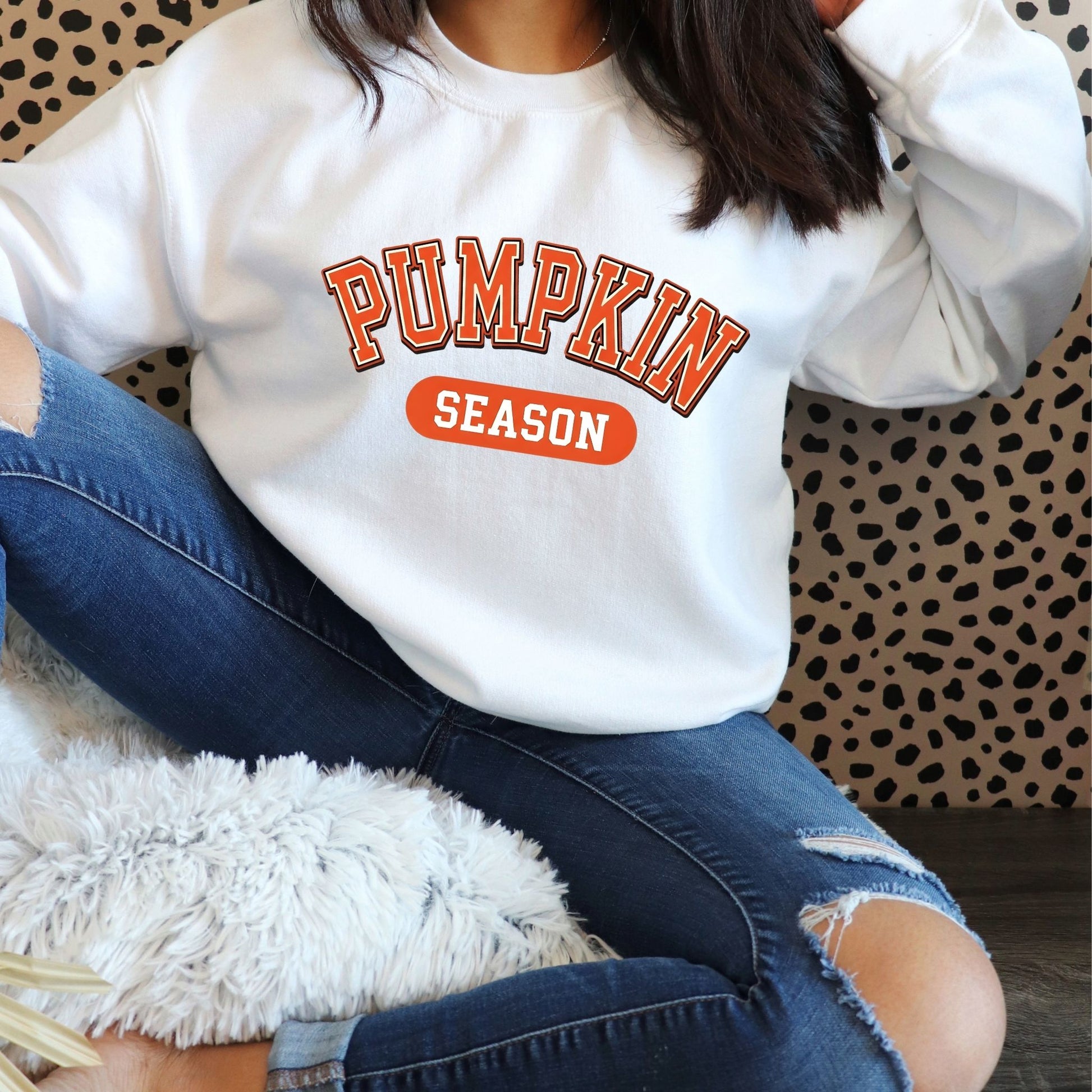 Person wearing a white sweatshirt with 'Pumpkin Season' text, sitting on a patterned chair.