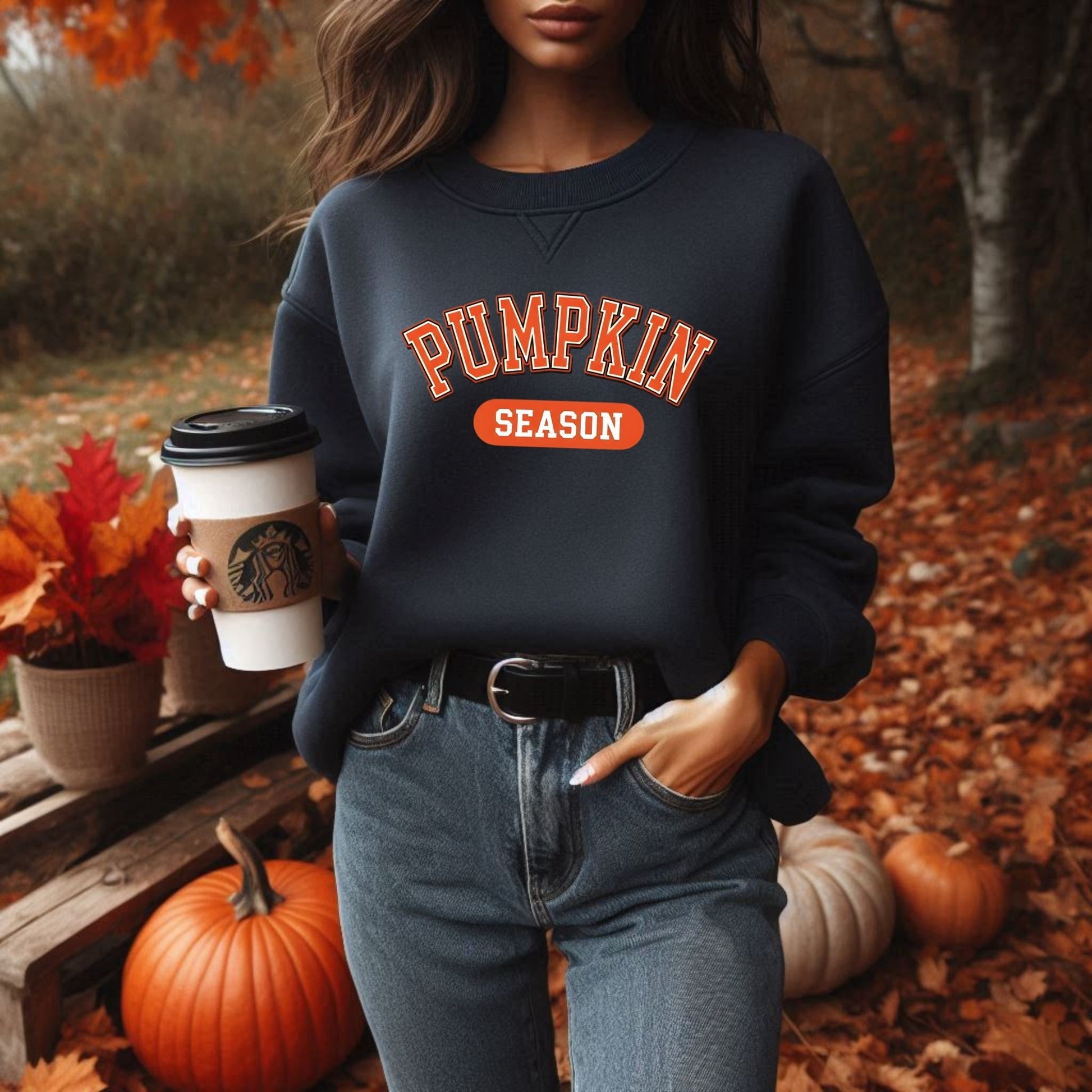 Person wearing a 'Pumpkin Season' sweatshirt holding a Starbucks cup in an autumn setting.