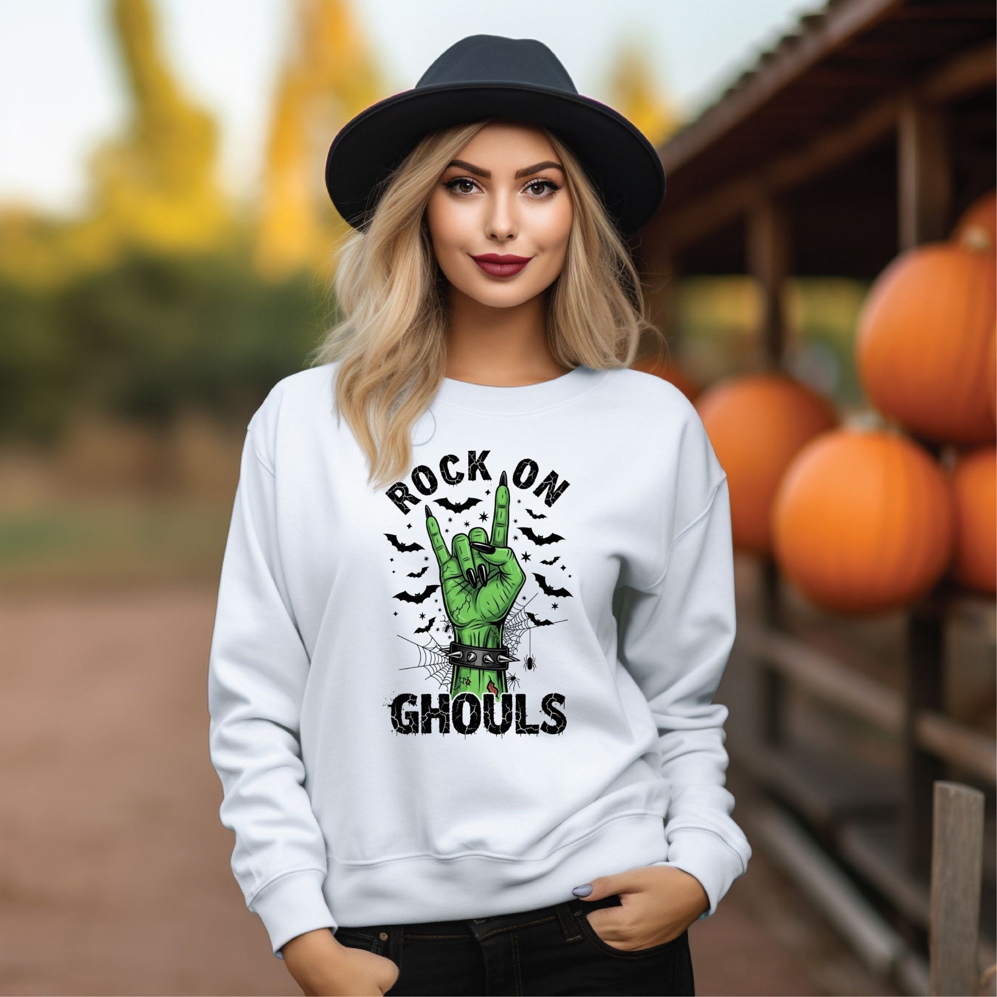 Woman wearing a white sweatshirt with a Halloween-themed design in an outdoor setting with pumpkins.