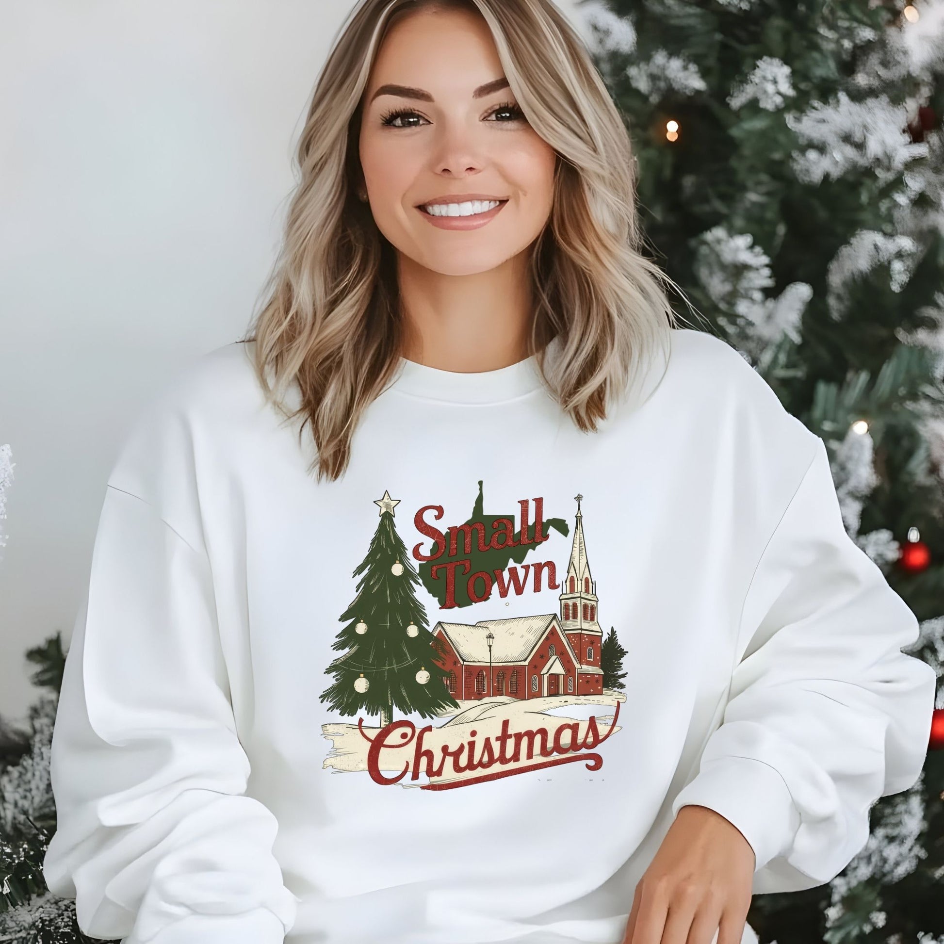 Woman wearing a white sweatshirt with 'Small Town Christmas' design in front of a decorated Christmas tree.