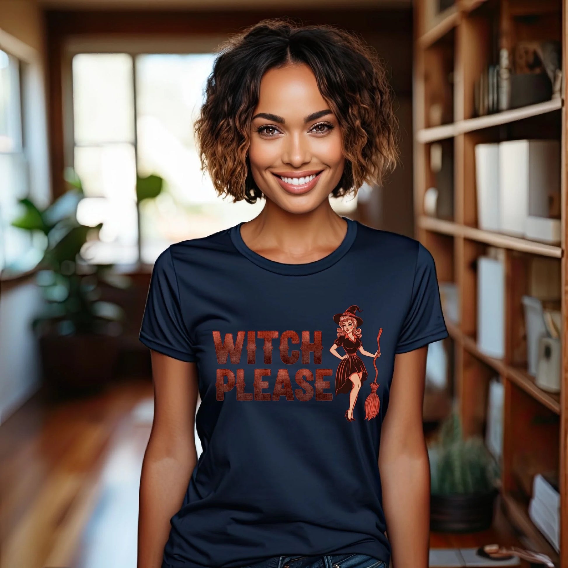 Woman wearing a navy blue t-shirt with 'Witch Please' graphic in a room with bookshelves and plants.