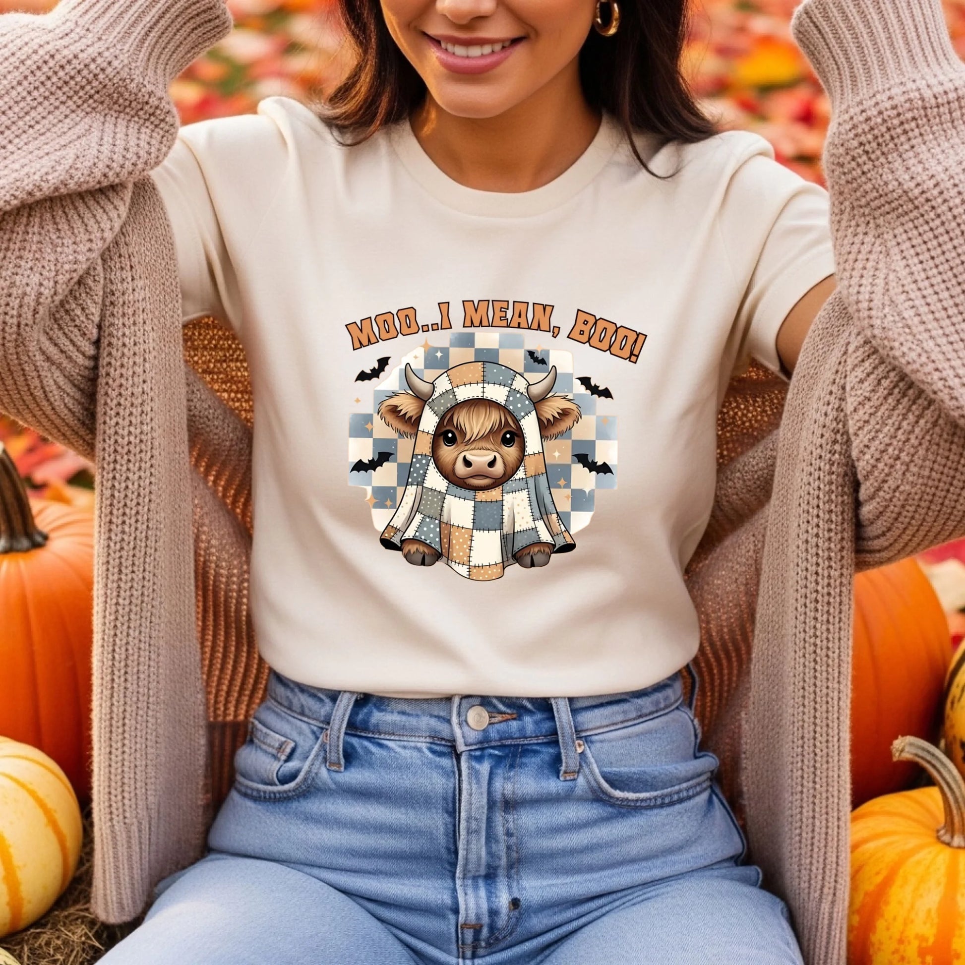 Person wearing a white t-shirt with a cow graphic and text, surrounded by pumpkins.