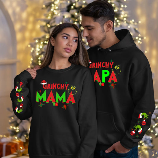 Two people wearing 'Grinchy Mama' and 'Grinchy Papa' hoodies in front of a decorated Christmas tree.