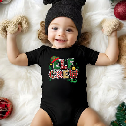 Child wearing a black 'Elf Crew' onesie on a white fluffy surface with Christmas decorations.