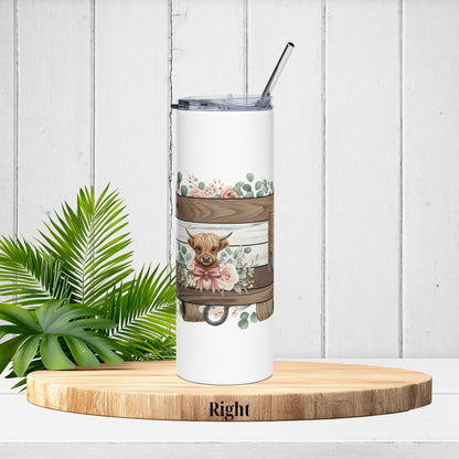 Right-side tumbler angle featuring the highland cow with floral bow sitting next to rustic planks and greenery.