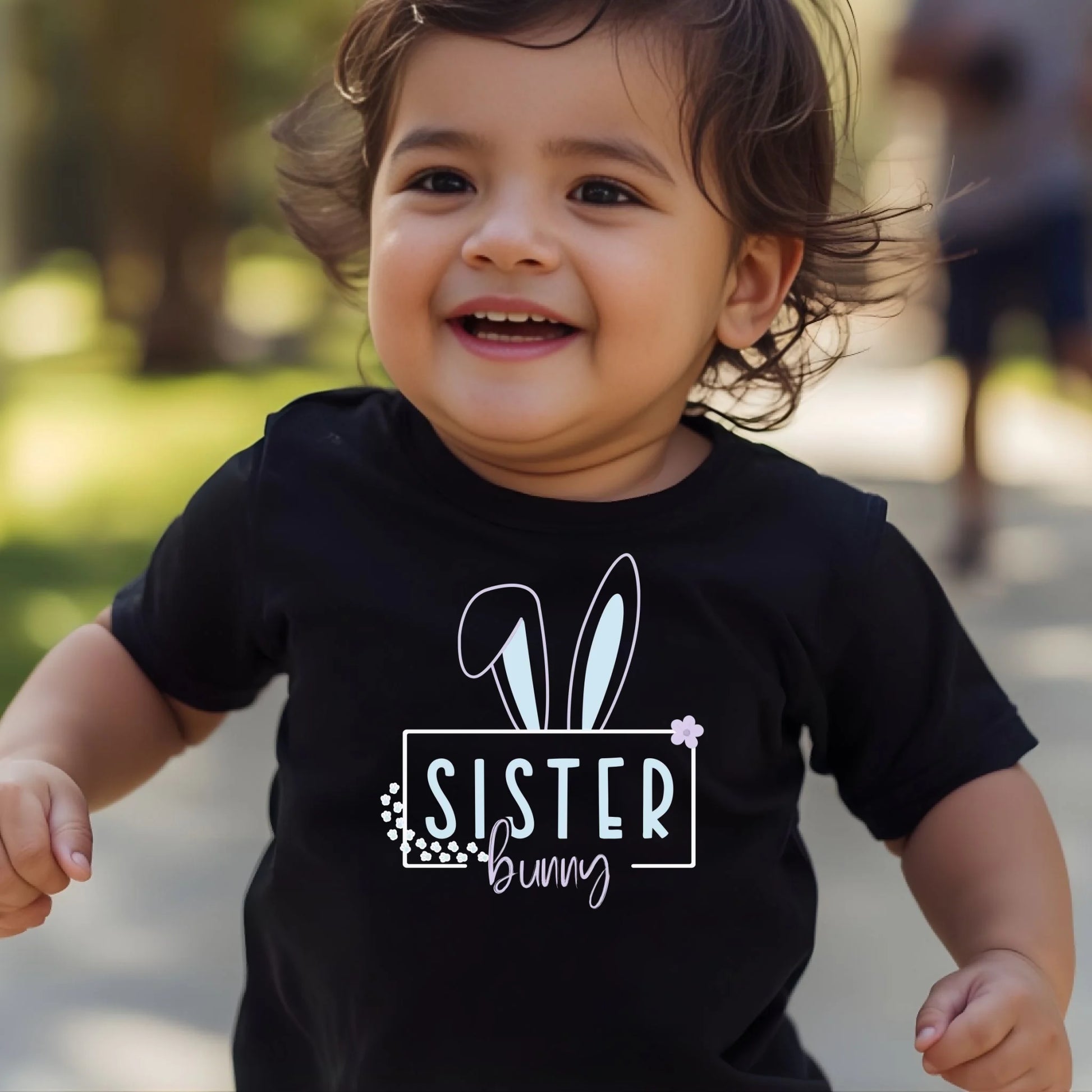 Smiling toddler wearing a black Easter bunny sister shirt during a playful outdoor moment.