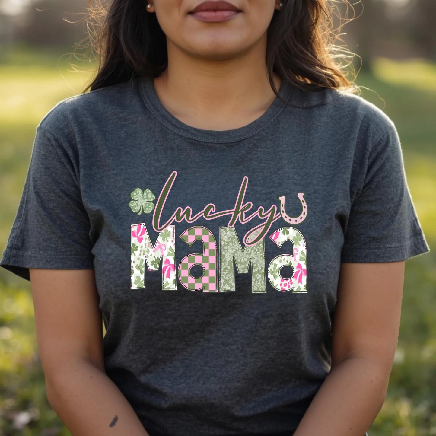 Person wearing a dark gray t-shirt with 'lucky mama' text in floral letters outdoors.
